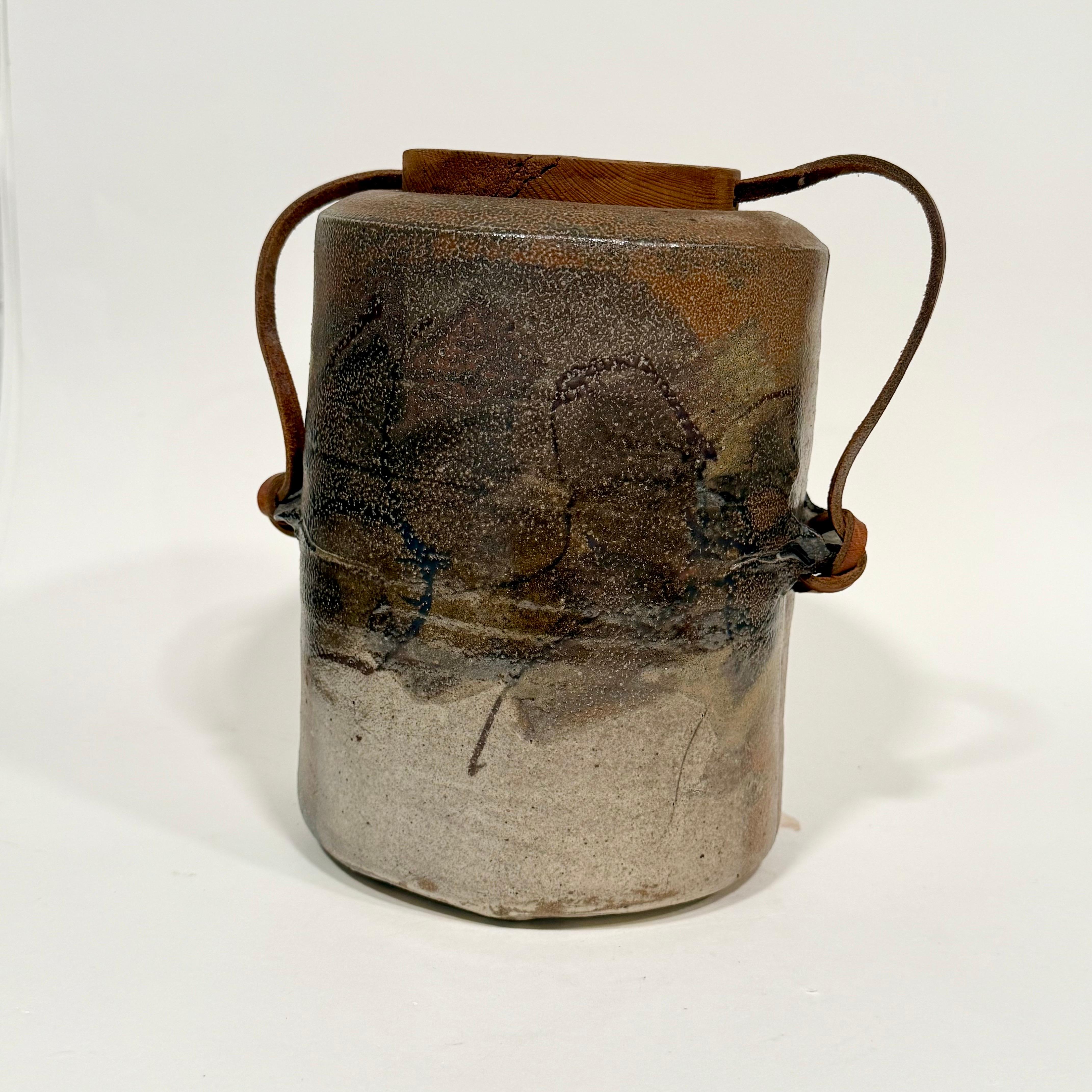 Asombrosa vasija abstracta con tapa, cocida con sal, de la alfarera Sandra Johnstone, c. 1970. Tapa de madera maciza con cordón de cuero que la sujeta al recipiente. Johnstone (1936-1991) estudió con Peter Voulkos en la Universidad de Berkeley a