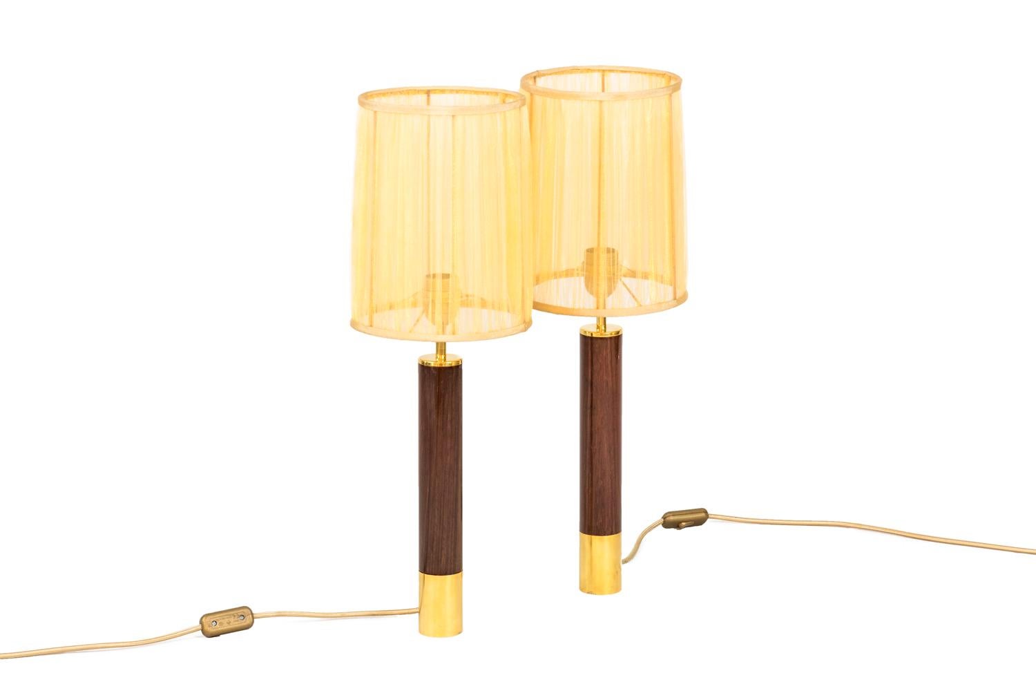 Santa & Cole, attributed to.
Pair of tubular shape “Basica” lamps in rosewood, surrounded by gilt brass ring on the bottom.

Work realized in the 1980s.

New and functional electrical system.

The price doesn’t include the lampshade price.