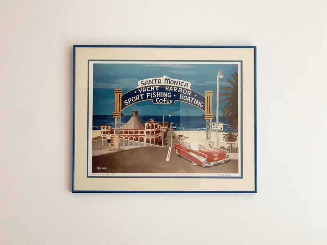 An offset lithograph after the original painting Santa Monica Pier 1957 by Stan Cline. This piece depicts Santa Monica Pier with beachgoers walking down the street and a vintage red Chevrolet car turning the corner. The piece is titled and signed by