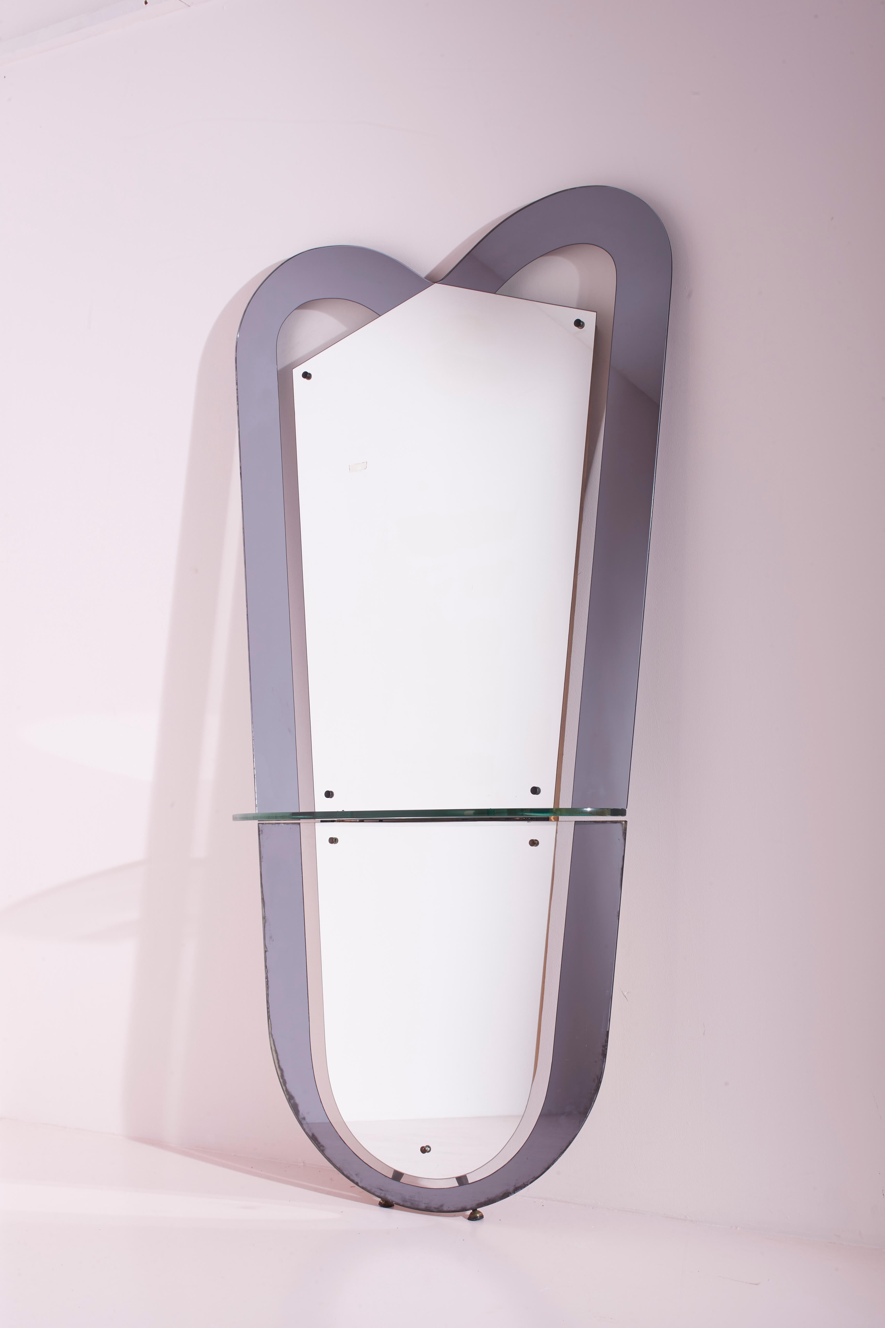 Grande console en miroir et verre coloré avec étagère en cristal, marque Santambrogio & De Berti, fabrication italienne des années 1965.

Le miroir de sol prend la forme d'un grand bouclier, composé d'un miroir entouré d'un cadre en verre miroir