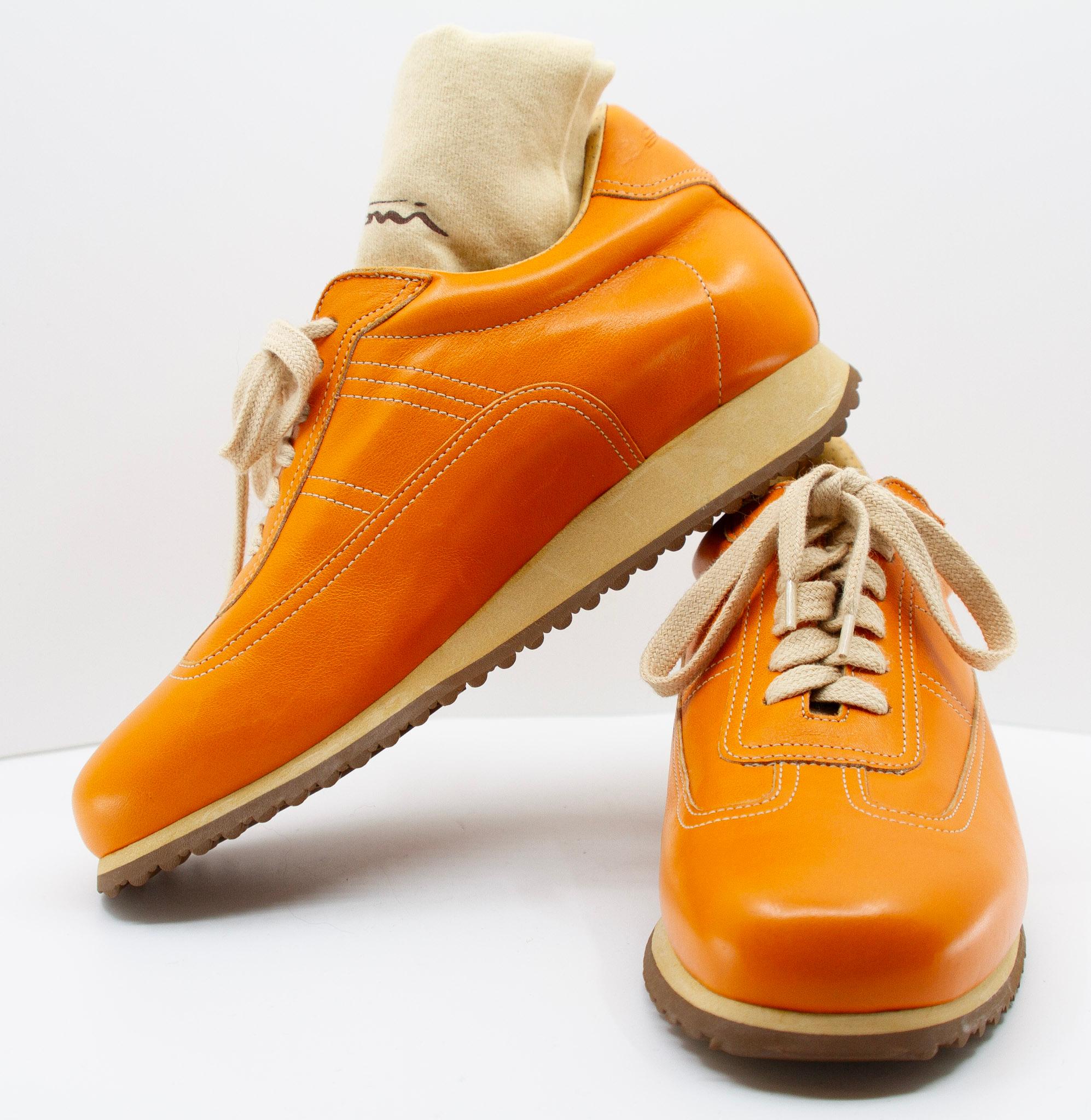  Zapatillas de piel naranja Santoni, talla 35. Estas zapatillas de fabricación italiana tienen la parte superior de piel naranja, puntera redondeada, pespuntes en contraste, cordones de color hueso, plantilla de piel y suela de color crema y marrón.