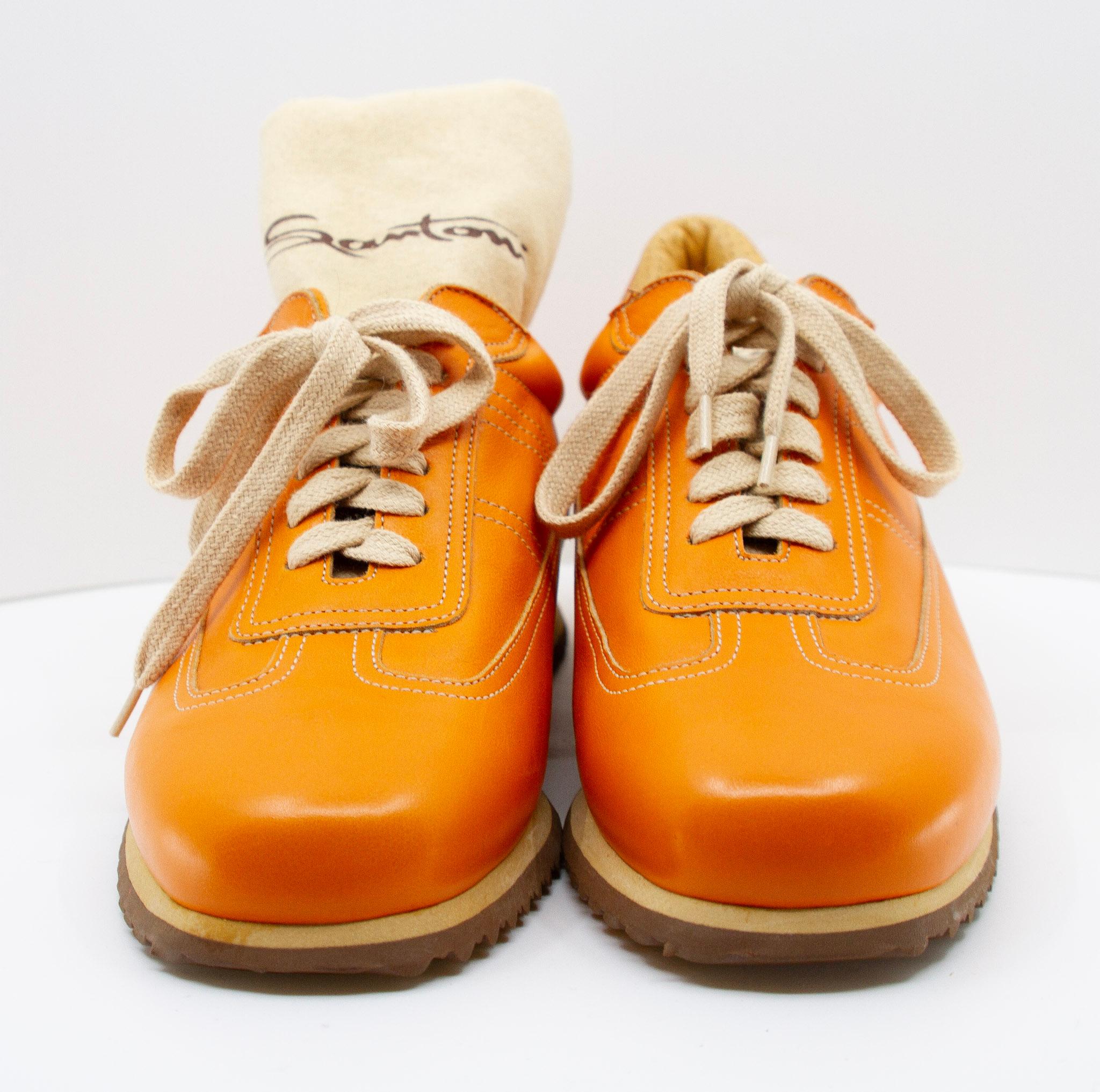  Santoni orange leather sneakers, in a size 35. These Italian made sneakers feature orange leather uppers, rounded toes, contrast stitching, off-white laces, leather insoles and cream and brown outsoles. Two Santoni drawstring dust covers are also