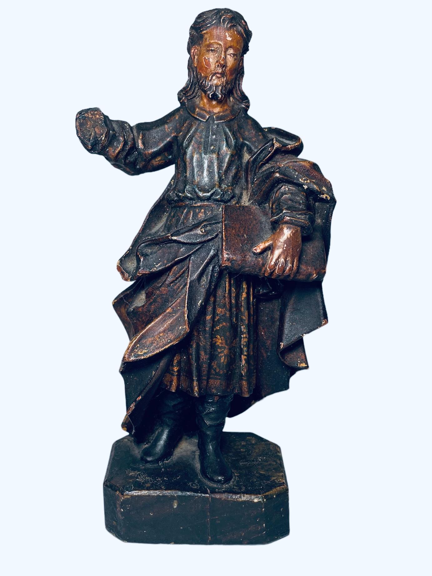 Questo è un Santos de Palos sconosciuto. Raffigura una scultura in legno scolpito a mano e policromato di un uomo che indossa una lunga tunica e stivali neri. Ha capelli lunghi, baffi e barba. Nella mano sinistra porta anche un grande libro