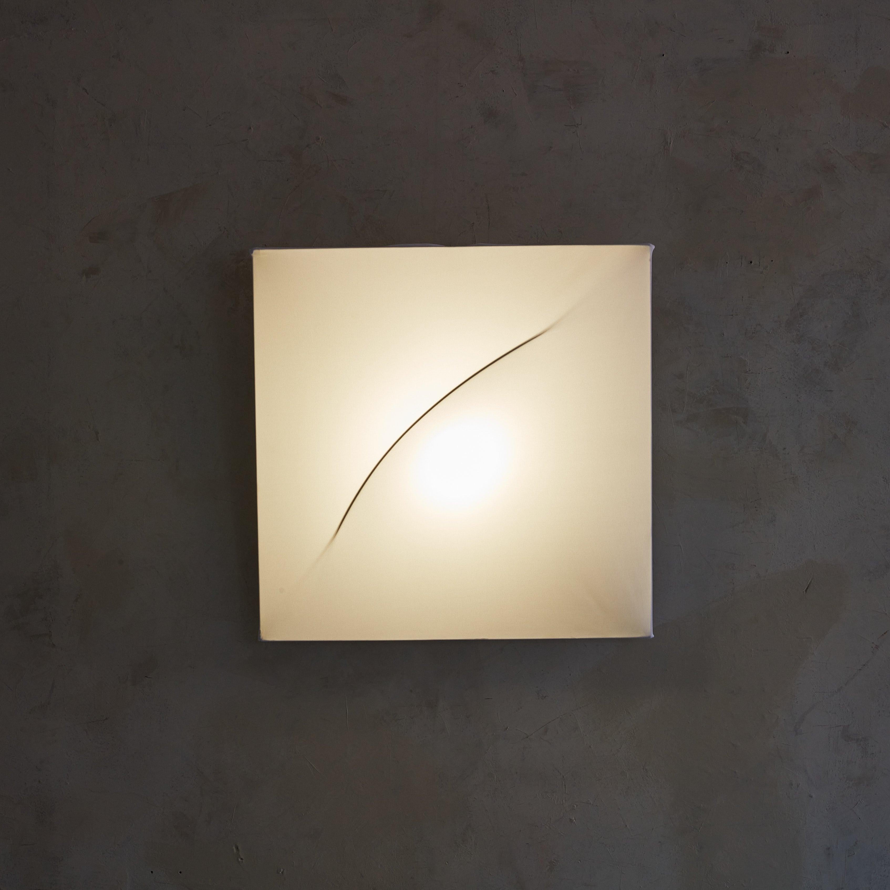An Italian Modern 'Saori' wall-mounted light fixture designed by Kazuhide Takahama for Sirrah in the 1970s. This light fixture’s square silhouette, composed of a metal frame enveloped in white jersey fabric, is distinguished by a central arc —