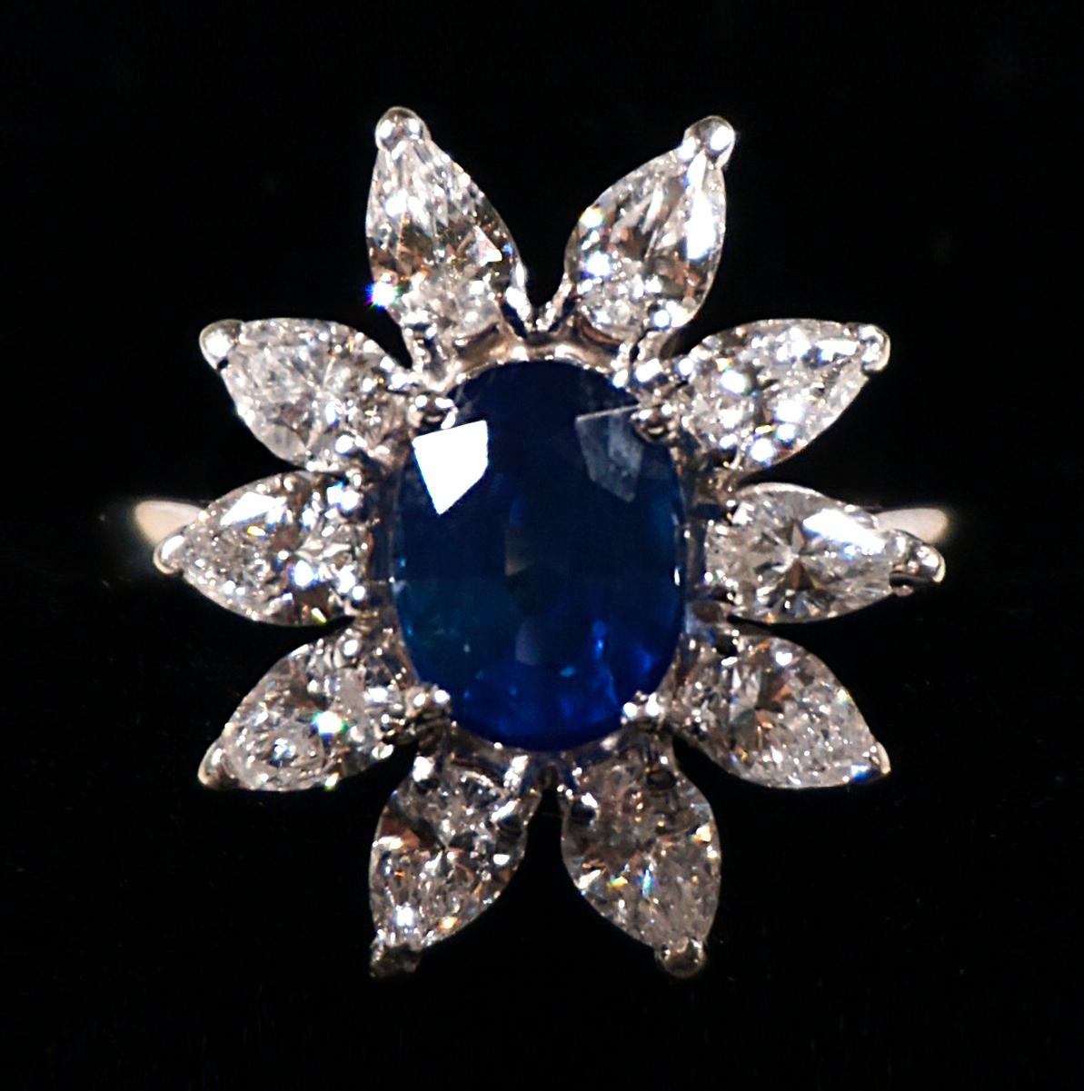 Classic flower-shaped sapphire and brilliant-cut diamonds ring with a centered facetted oval saphire, surounded by 10 drop-shaped cut diamonds estimated to weigh a total of 1.8 carat, claw set in a 18k white gold mount.
 
Circa 1970

head measuring 