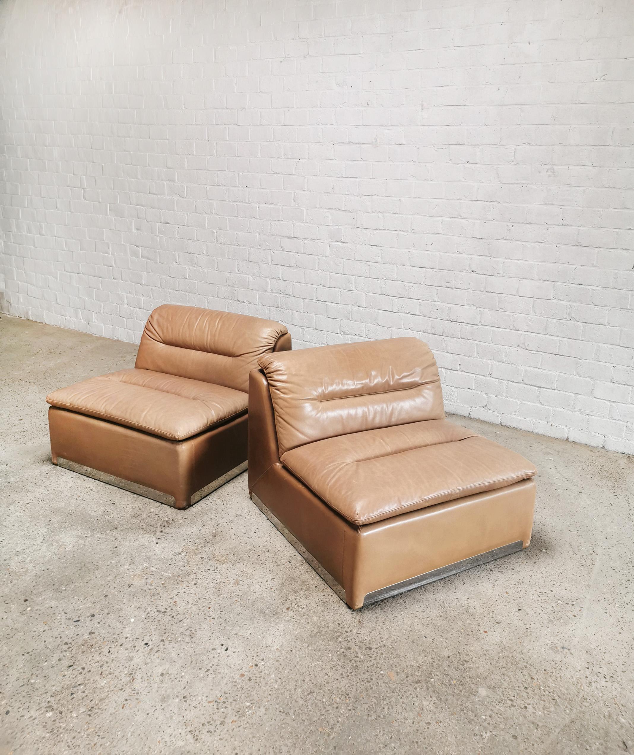 A pair of 1970's saporiti 'P10' modular lounge chairs, upholstered in the original rich cognac leather. These lounge chairs feature a heavy upholstered steel base frame, with an L shaped seat, and armless modular design. Their modernist style