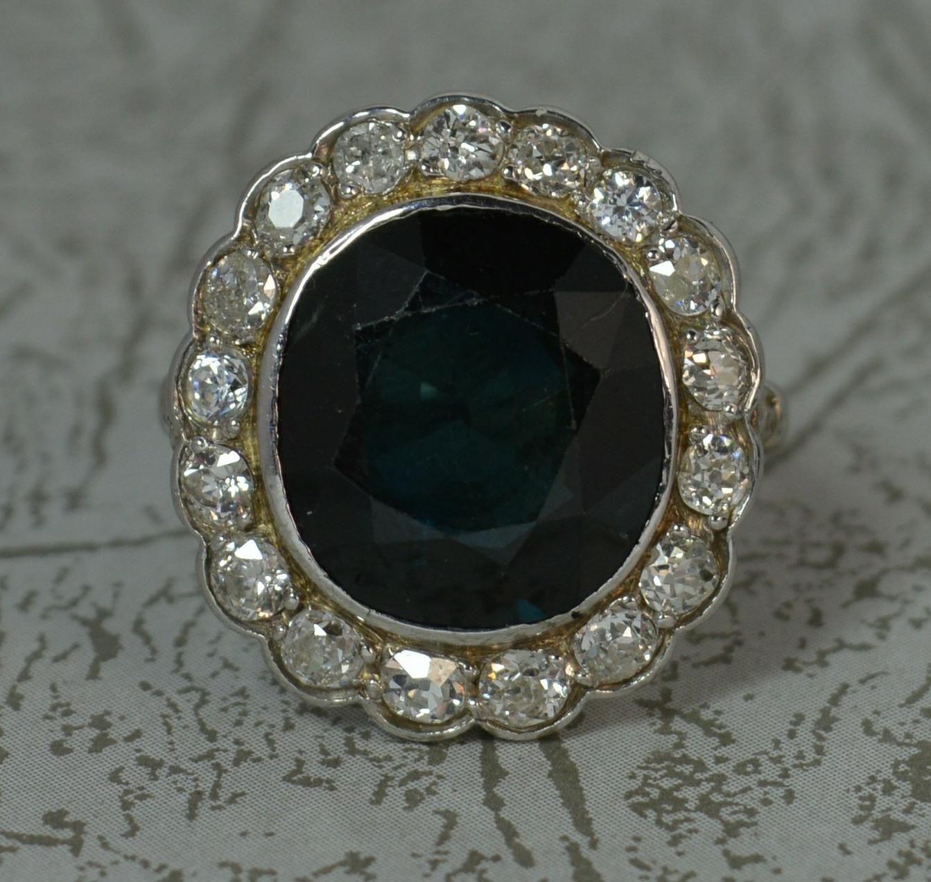 A beautiful true antique cluster panel ring. c1930.
Solid 18 carat white gold example.
Designed with a large oval cushion dark blue / green sapphire. Measures approx 12.4mm x 13.3mm x 4.2mm approx.
Surrounding are seventeen natural old cut diamonds