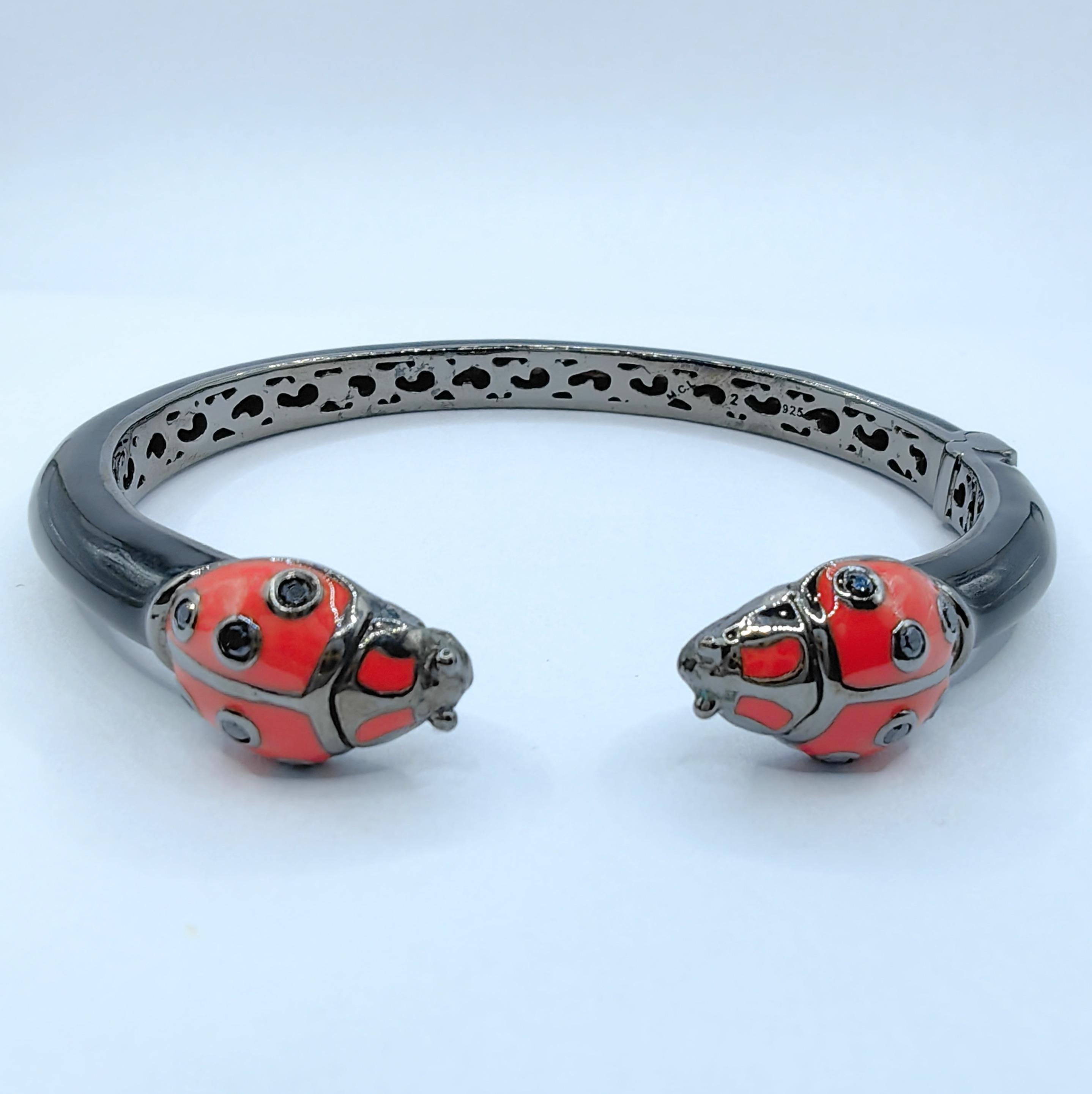 Wir präsentieren das Sapphire Adorned Ladybugs Rounded Thin Cuff Bracelet aus emailliertem Sterling Silber, ein charmantes und skurriles Stück, das Ihrer Schmucksammlung einen Hauch von Spaß verleiht. Diese entzückende Manschette aus Sterlingsilber