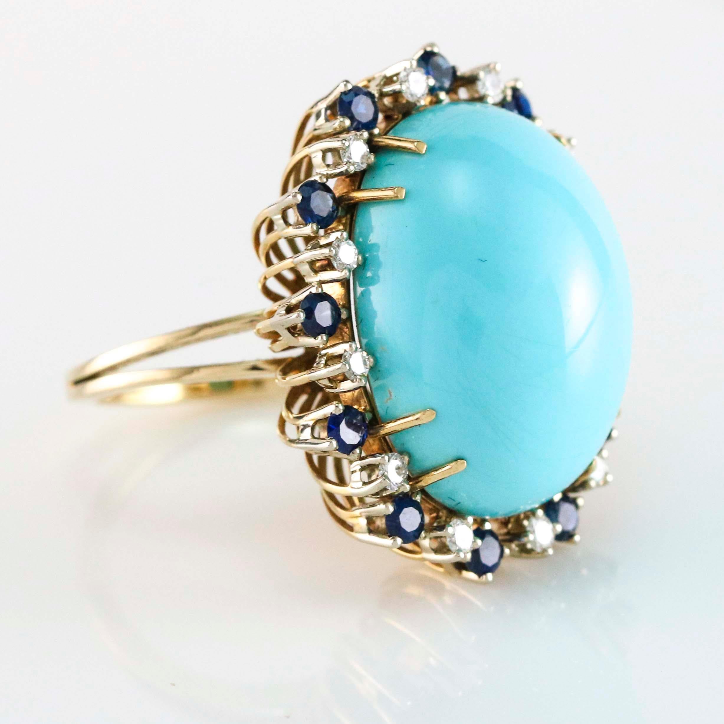 Turquoise cocktail ring in 18 karat yellow gold with natural blue sapphires and diamonds. The ring has a large oval turquoise center stone with 12 natural blue sapphires, and 12 round diamonds around. Size 7.5. Turquoise, 23mm x 17mm.