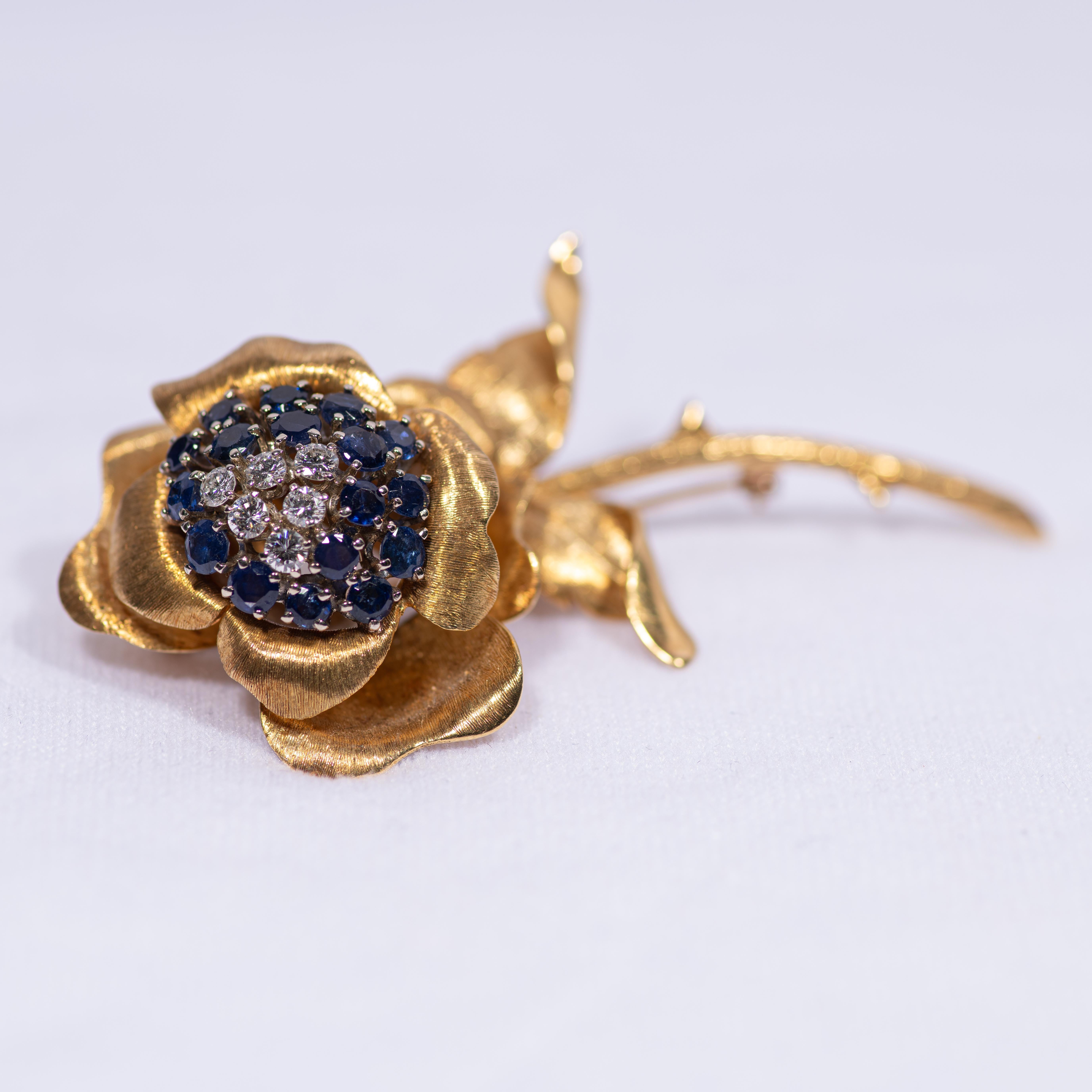 A fine and heavy flower brooch in the form of a stemmed rose. The rose's petals, stem and thorns crafted in textured Florentine finished yellow gold, with pistils of blue sapphire, and stamen of diamonds. 

The center of the rose embellished with 17