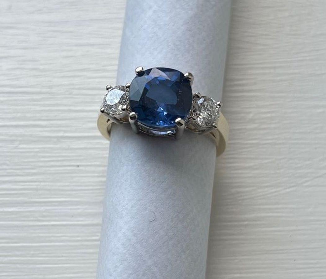 Simply Beautiful! Finely detailed Three Stone Sapphire and Diamond 3-Stone Gold Cocktail Ring. Centering a securely nestled Hand set Cushion Cut 4.41 Carat Blue Sapphire, eye clean clarity, extra fine color grade. Measuring approx. 9.37 x 9.31 x