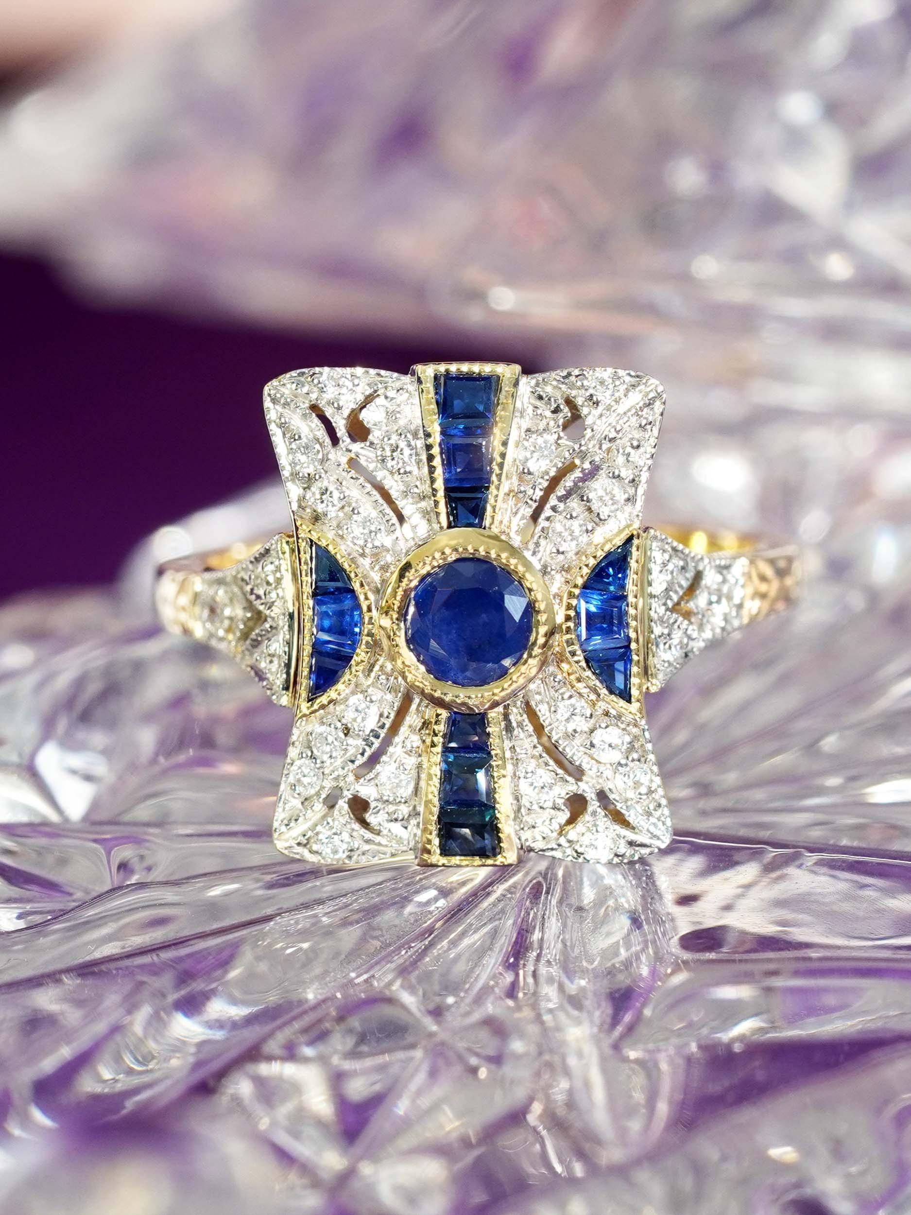 Embrassez la sophistication classique avec cette bague de fiançailles en saphir et diamant de style Art déco. Un saphir rond trône audacieusement au centre, entouré d'un halo de diamants scintillants dans un design cible saisissant. Flanqués de
