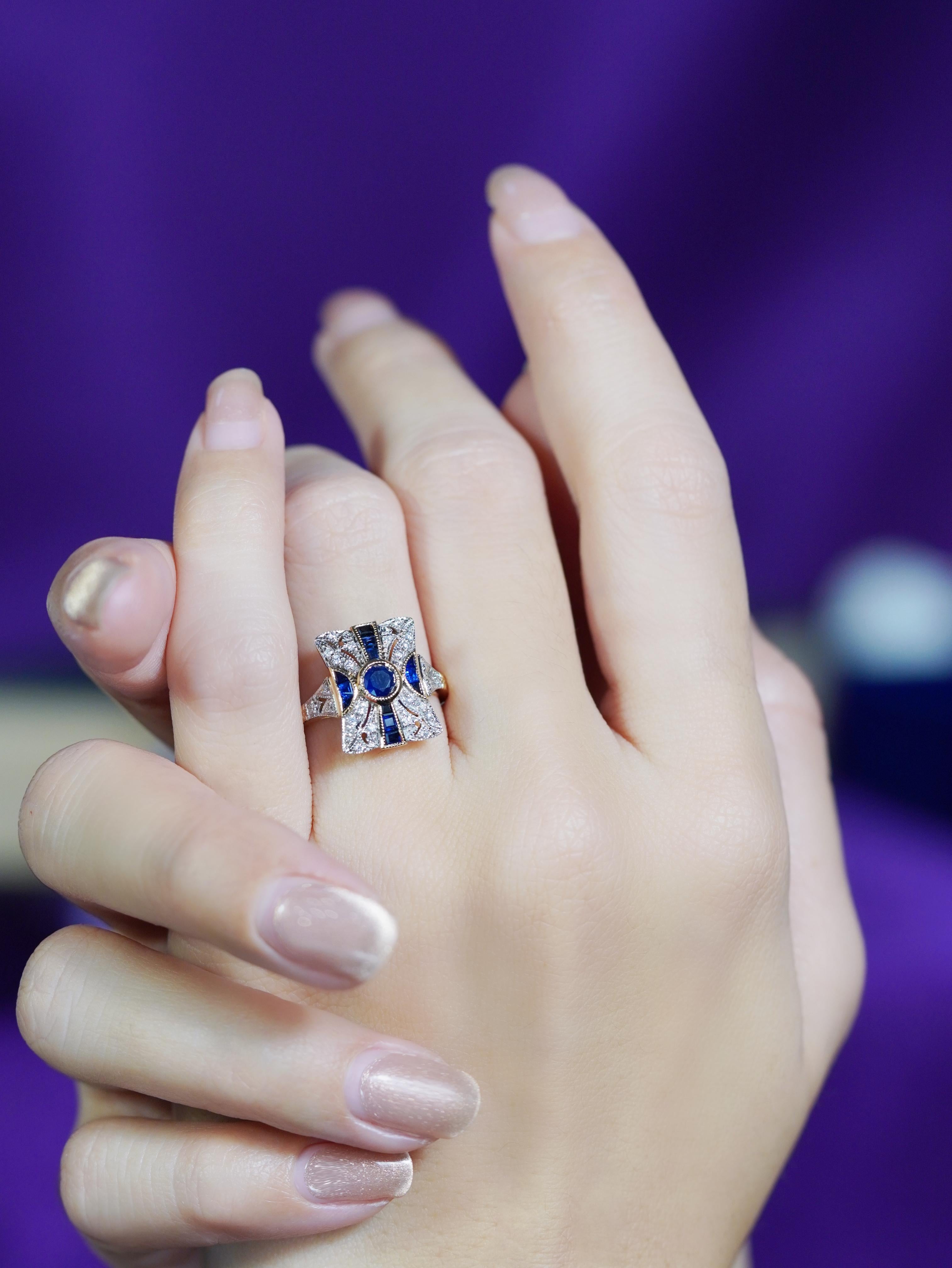 Embrassez la sophistication classique avec cette bague de fiançailles en saphir et diamant de style Art déco. Un saphir rond trône audacieusement au centre, entouré d'un halo de diamants scintillants dans un design cible saisissant. Flanqués de