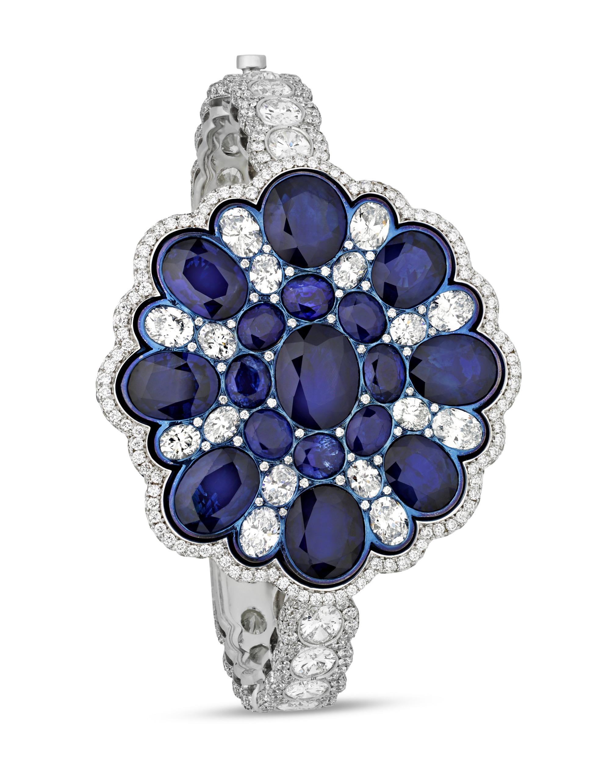 This stunning bangle bracelet is a symphony of sapphires. Featuring nine large sapphires totaling 27.29 carats, it is also adorned with one hundred smaller sapphires weighing 6.00 carats. White diamonds totaling 21.98 carats accentuate the
