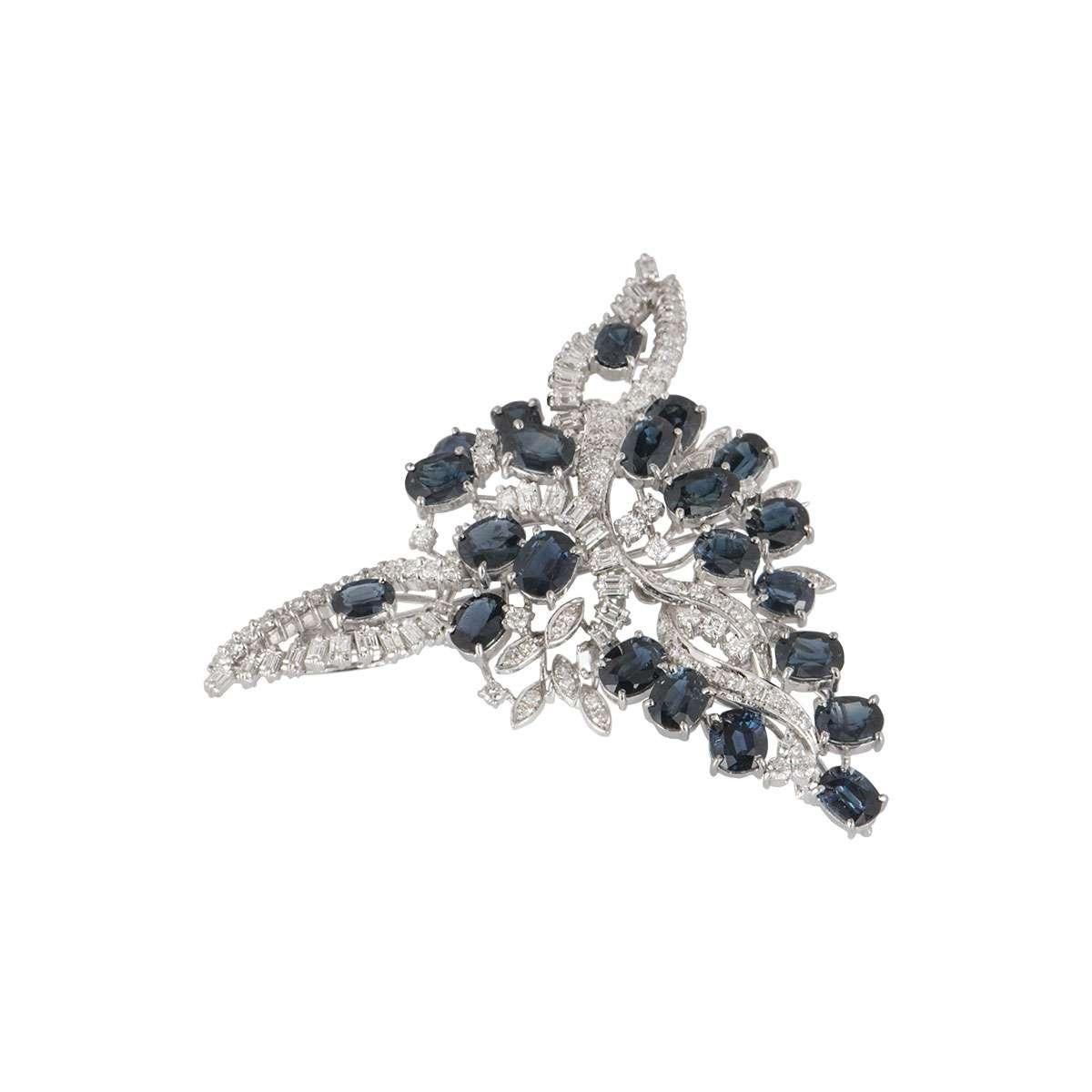 A stunning white gold sapphire and diamond brooch. The openwork brooch is set with 22 mixed oval and round cut sapphires totalling approximately 12.35ct, displaying a deep blue colour. Complementing the sapphires are baguette and round brilliant cut