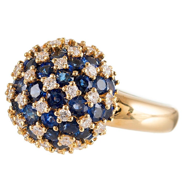 An orb of intense blue sapphires and brilliant white diamonds is assembled atop an 18 karat gold ring. The piece is fun playful, with a ton of punch. The sapphires weigh 5.61 carats and the diamonds weigh .93 carats in total. Size 6 can be resized