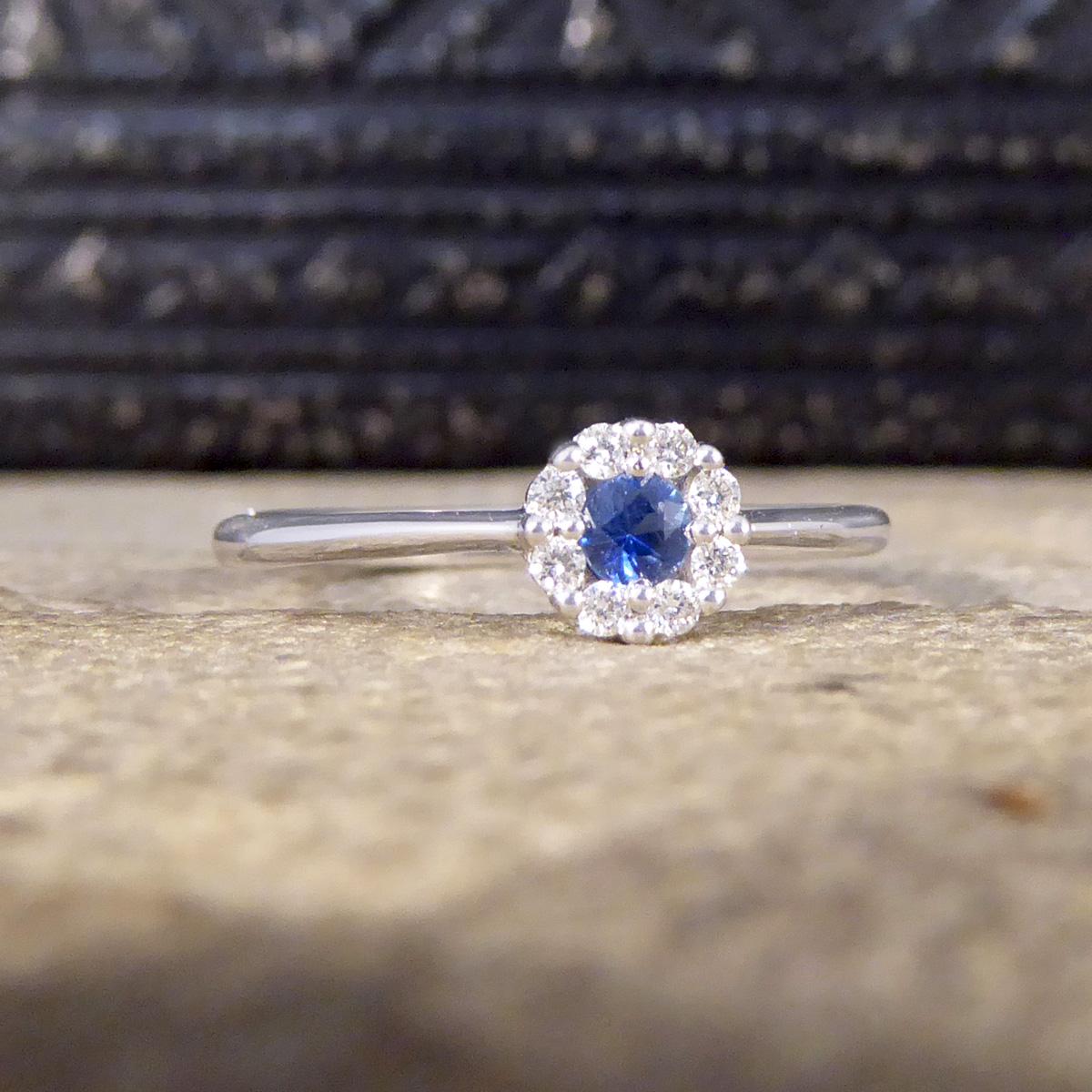 This lovely little ring has the perfect balance of elegance and quality. Crafted using 18ct White Gold this ring features a beautifully blue Sapphire in the centre weighing 0.11ct with a cluster surround of 0.08ct Brilliant Cut Diamonds set in