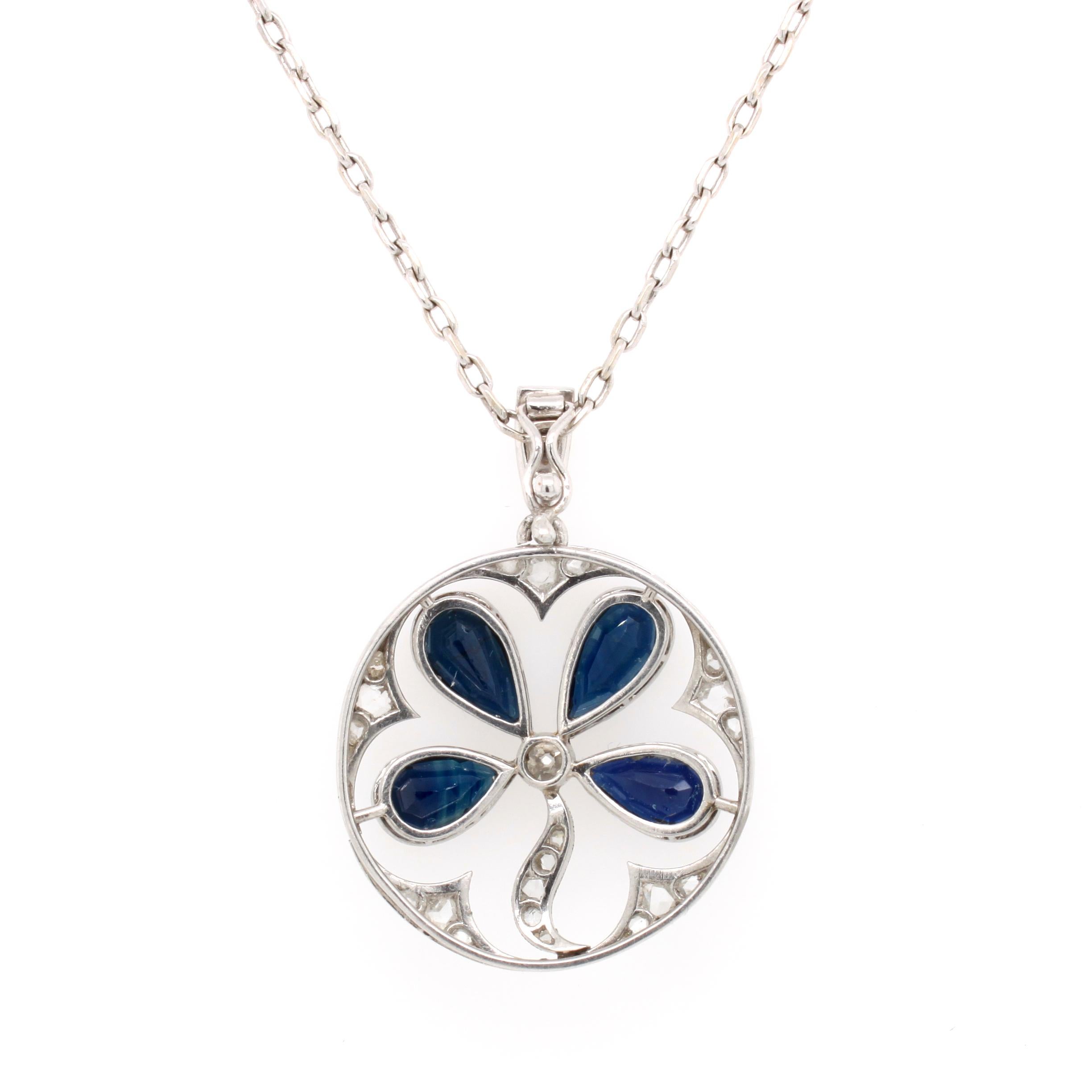 A sapphire and diamond clover or trefoil pendant in platinum, ca. 1910s, Belle Époque. This round pendant has a four leaf clover depicted in the center made out of four sapphire pear shapes, which are surrounded by rosecut diamonds. The four leaved