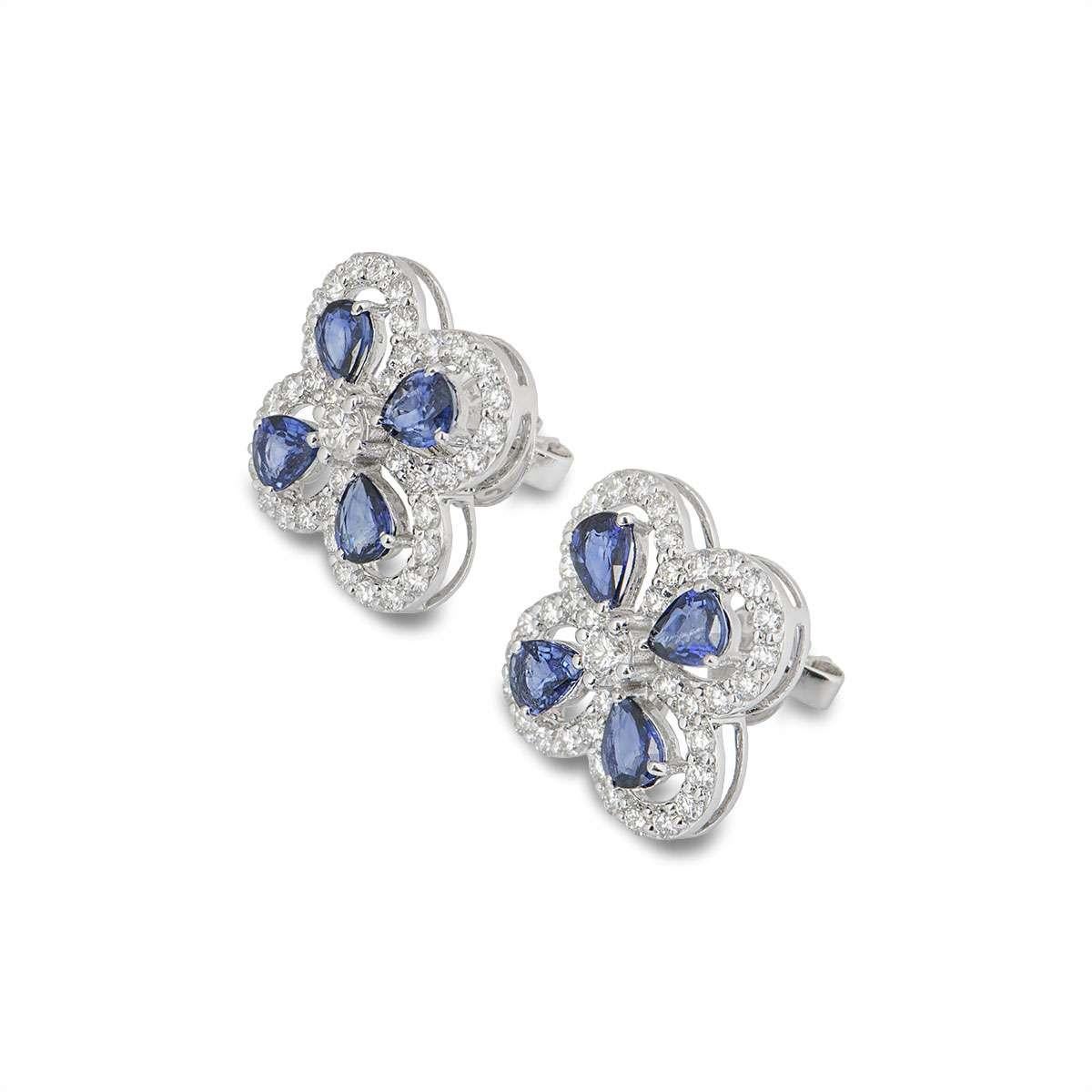 A pair of 18k white gold sapphire and diamond earrings. The openwork earrings are each set with 4 pear cut sapphires surrounding a single claw set round brilliant cut diamond. The outer boarder is pave set with round brilliant cut diamonds. The