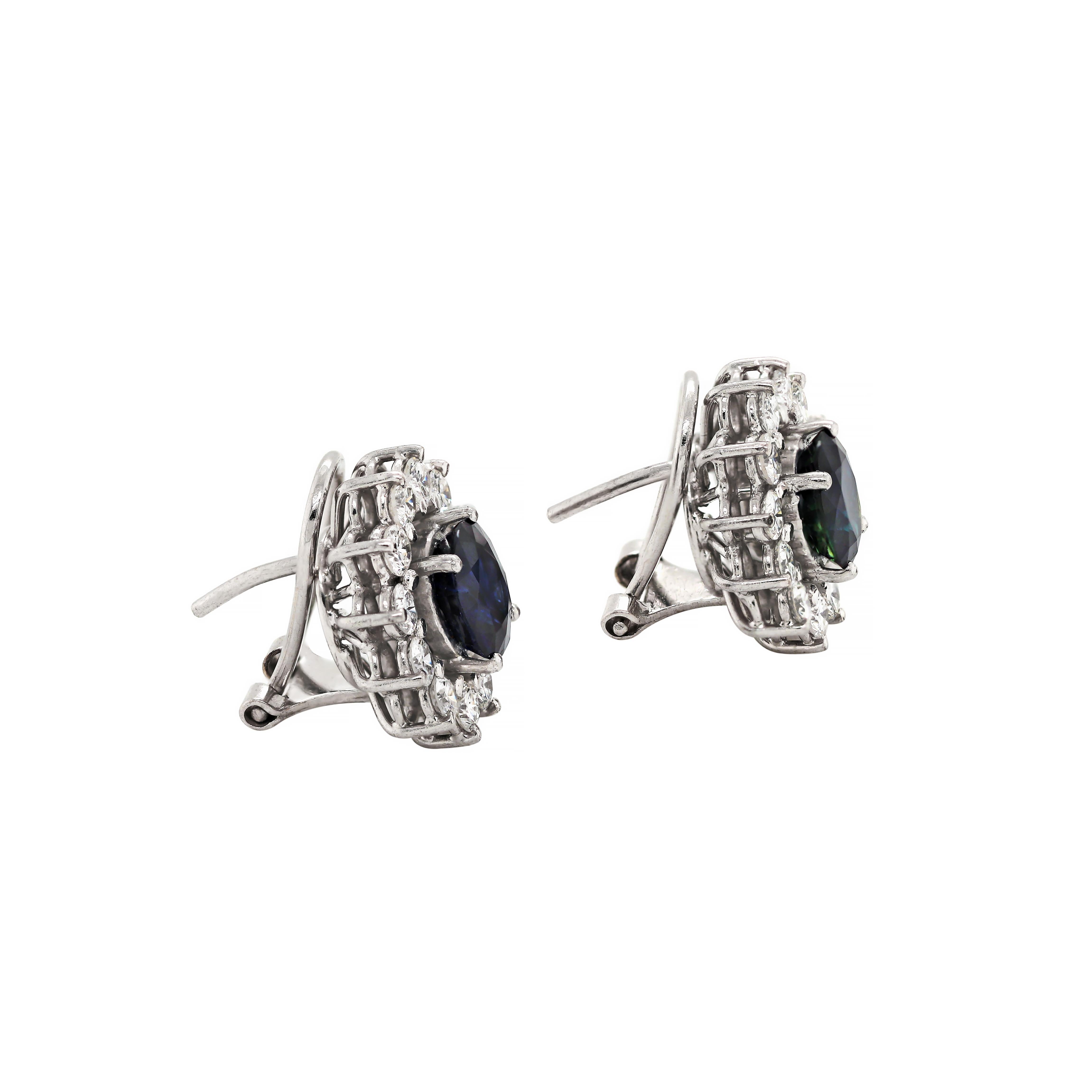 These classic cluster earrings feature an oval natural blue sapphire mounted in open back, four claw settings, weighing an approximate combined weight of 4.50ct. The sapphires are beautifully surrounded by 12 round brilliant cut diamonds, also claw