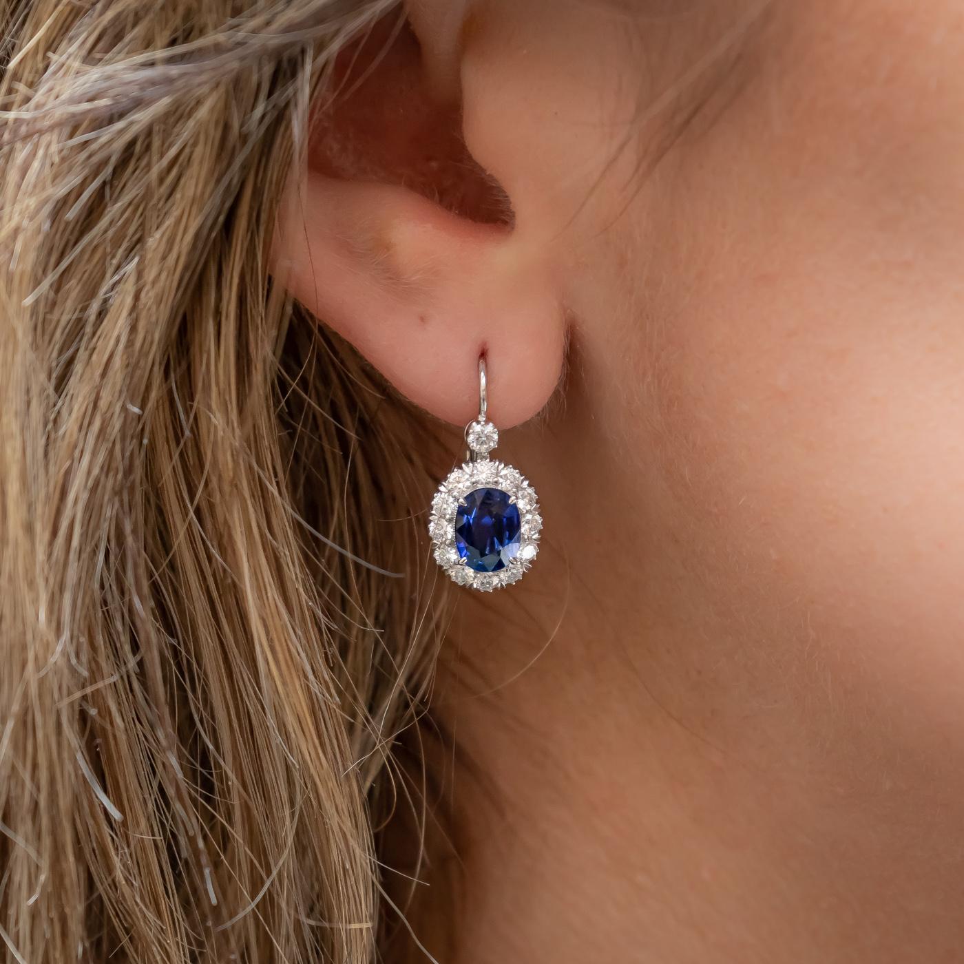 A pair of sapphire and diamond cluster earrings, each set with an oval faceted sapphire, with a total weight of 2.64ct, surrounded by a cluster of round brilliant-cut diamonds and a single diamond above, with a total diamond weight of 1.06ct,