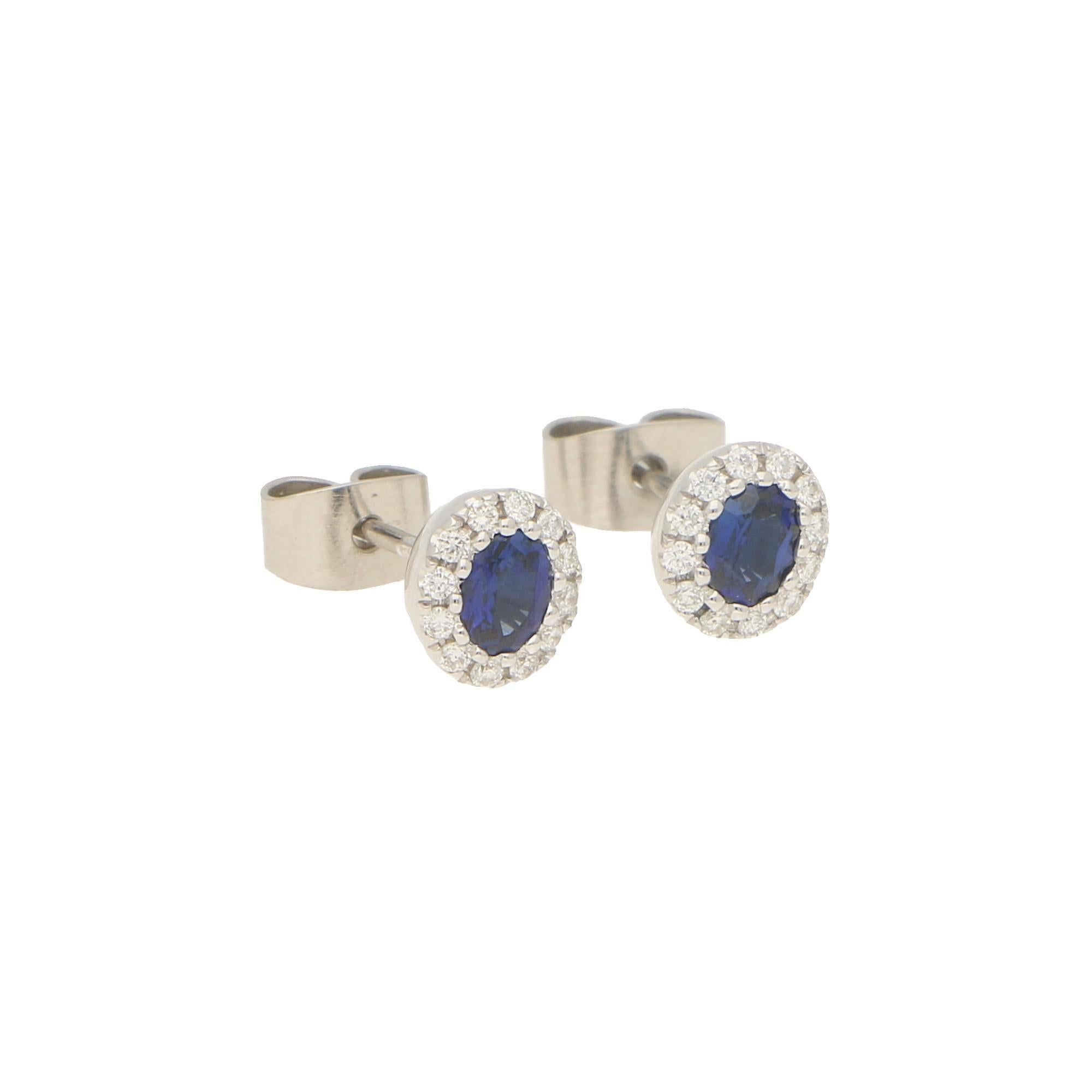 A lovely pair of petite sapphire and diamond oval halo earrings set in 18k white gold. 

Each earring centrally features a royal blue coloured oval shaped sapphire surrounded by a halo of 12 round brilliant-cut diamonds. All of the stones are set to