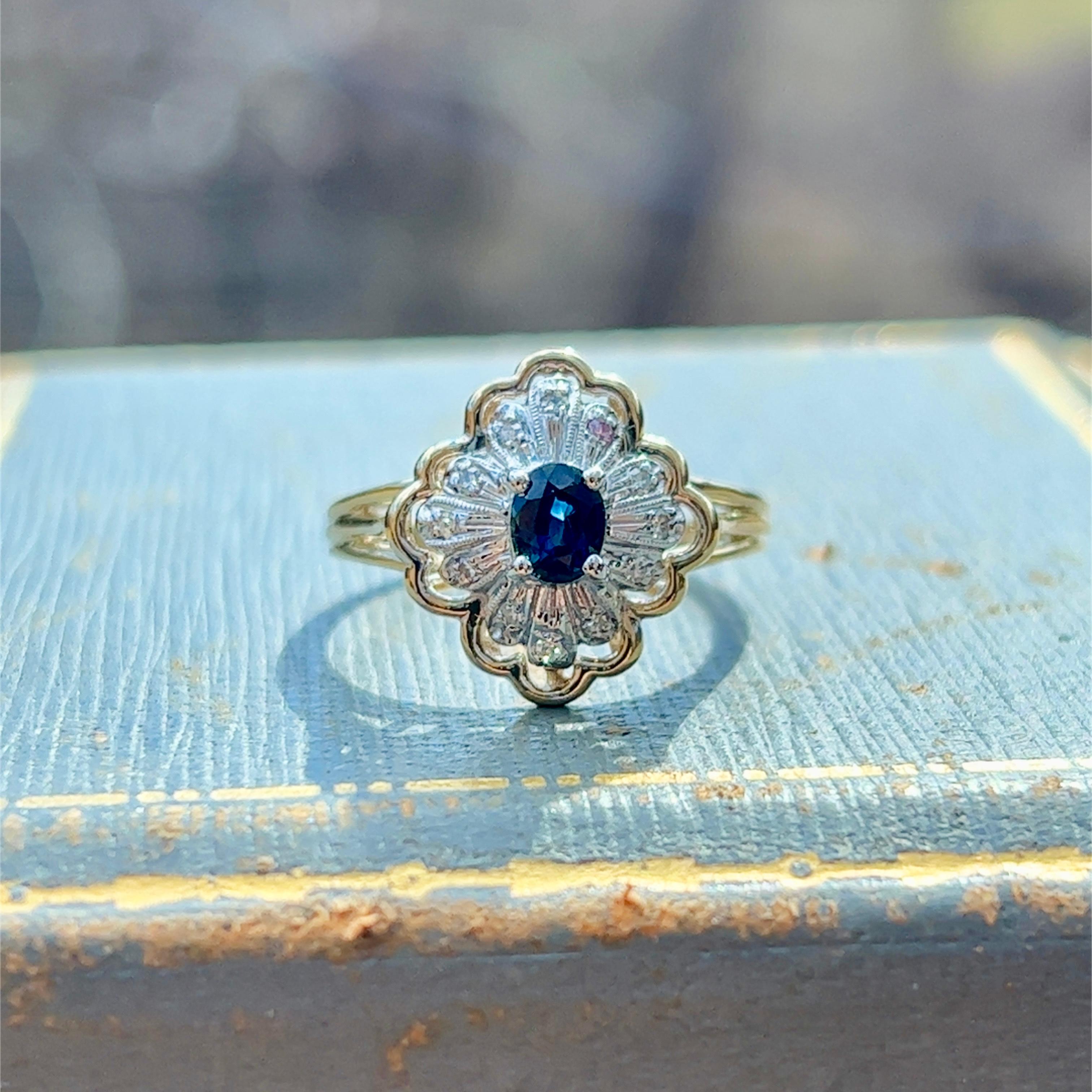 One 14-karat yellow and white gold cluster ring set with one  (1) 5x3.8mm oval natural blue sapphire, and twelve (12) single cut diamonds, approximately 0.20-carat total weight with matching H/I color and SI1 clarity. The ring is a finger size 7.5