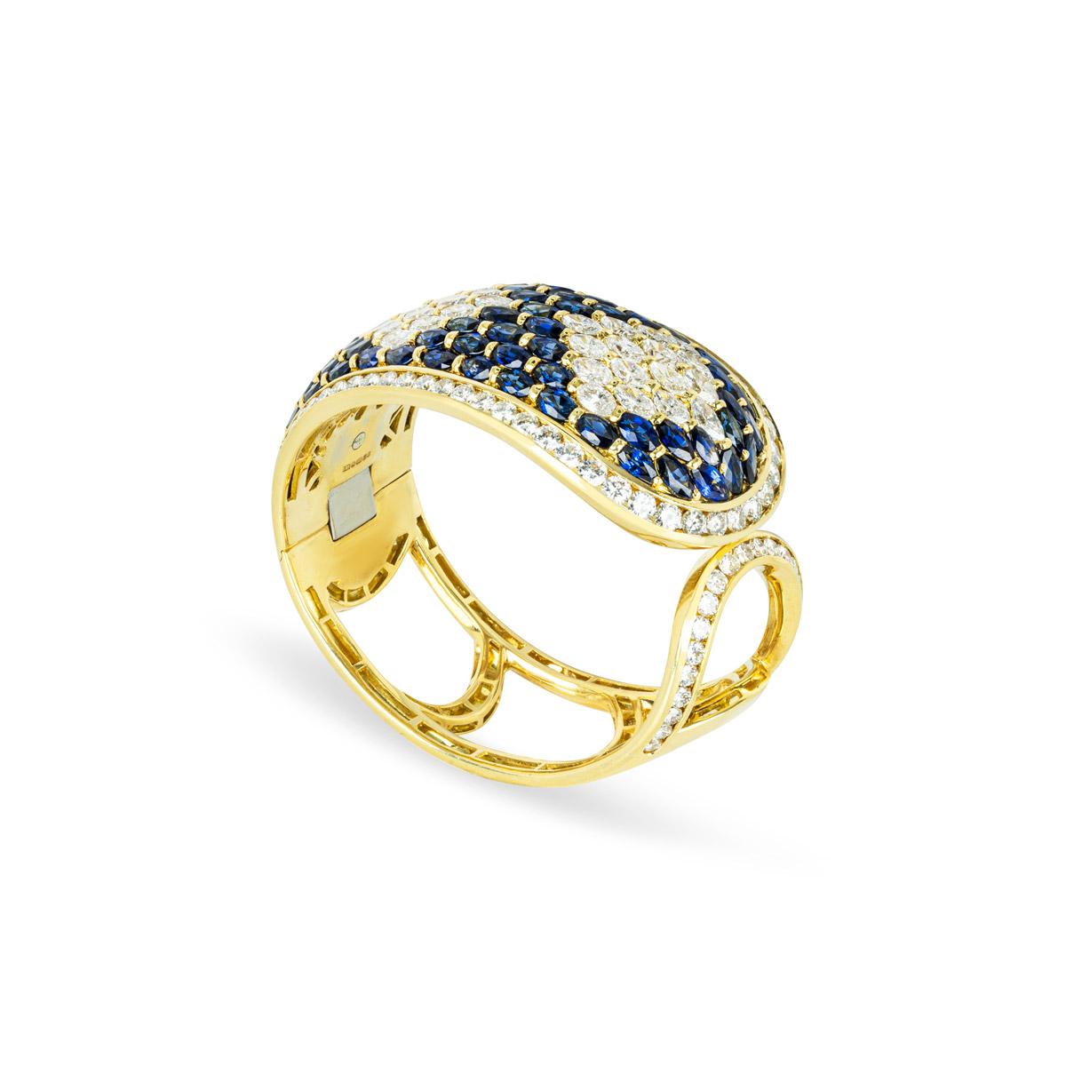 A stunning 18k yellow gold sapphire and diamond cuff bangle. The bangle comprises of a cuff style encrusted with 40 marquise cut diamonds forming 3 diamonds shaped illusion. Complementing this are 73 marquise cut sapphires around with round