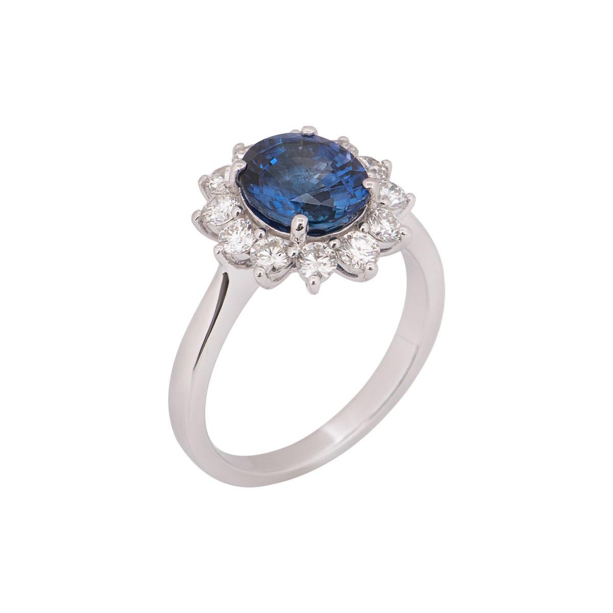 An 18k white gold sapphire and diamond ring. The ring is set to the centre with a 2.80ct oval cut sapphire, accentuated by a halo of 12 round brilliant cut diamonds totalling 0.80ct. The ring is currently a UKsize N½, US 6 3/4 but can be adjusted