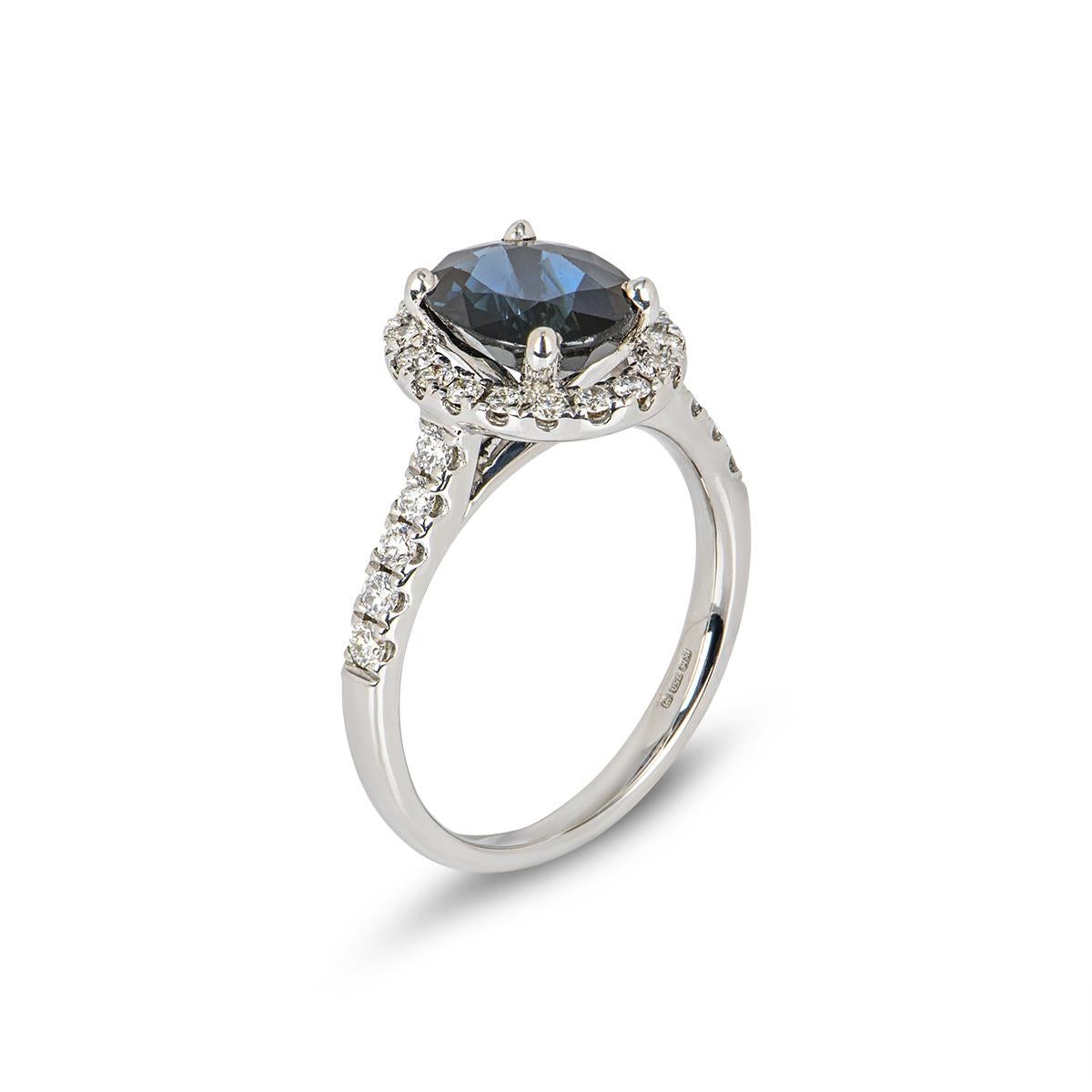 A sapphire and diamond cluster ring set in 18k white gold. This vintage inspired design is set to the centre with an oval faceted sapphire, claw set within a diamond halo surround and diamond set shoulders. The 28 round brilliant cut diamonds total