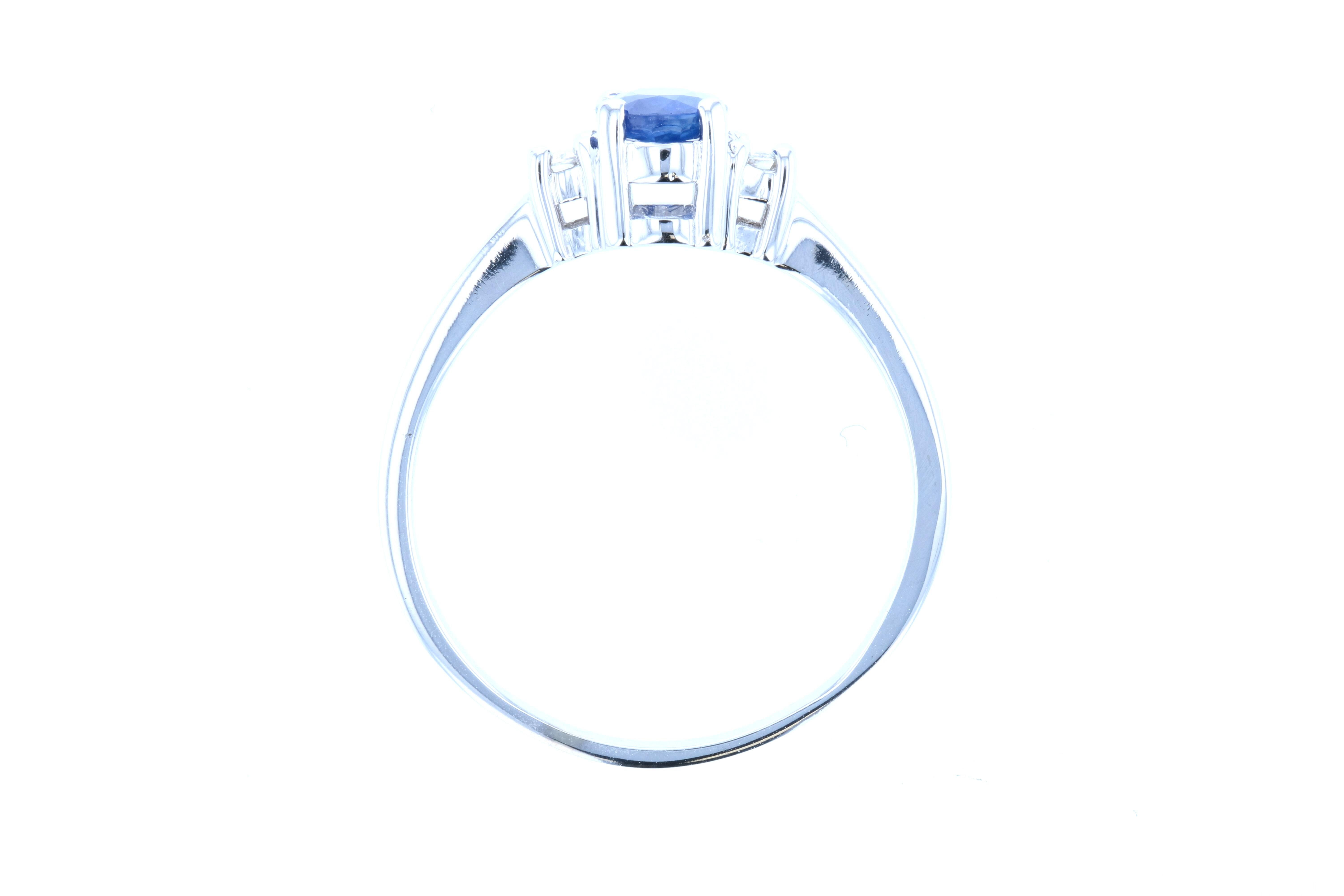 This gorgeous round blue sapphire engagement ring is further elevated by the addition of two tapered, emerald diamond baguettes on either side of the center stone. Set in white gold with a slightly raised profile, this stunning engagement ring