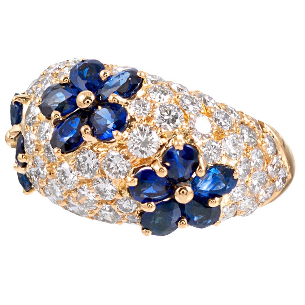 A gentle dome shape of 18 karat yellow gold is decorated with intense blue pear brilliant sapphires with their striking color highlighted by bright white diamonds. The sapphire petals are fashioned into perfectly symmetric flowers, the trio of three