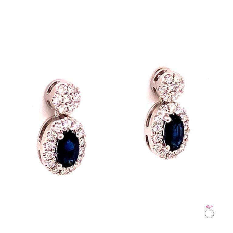 Sapphire and diamond halo small drop earrings in 14k white gold. The earrings feature two beautiful oval blue sapphires, surrounded by diamond halos and suspended from a diamond cluster stud. Each sapphire is approximately 0.35 carats. There are a