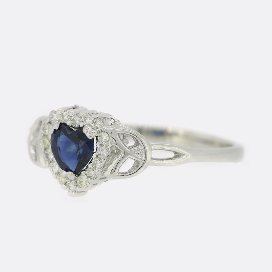 Ecco un anello a grappolo con zaffiri e diamanti in oro bianco 14ct. Lo zaffiro centrale a forma di cuore è sollevato in una montatura a griffe e intorno ad esso ci sono 16 diamanti rotondi taglio brillante in una formazione a grappolo. Lo zaffiro