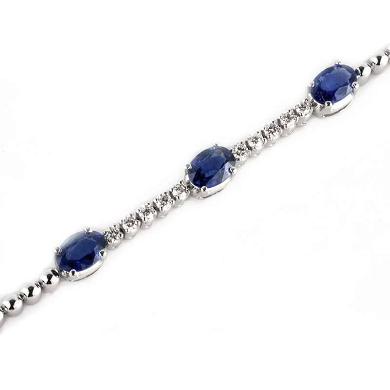 A classic 18k white gold sapphire and diamond line bracelet. The bracelet comprises of a beaded bracelet, intermittently set with 9 claw set, oval sapphires totalling 4.75ct, with a deep royal blue hue evenly dispersed. Complementing the centre of