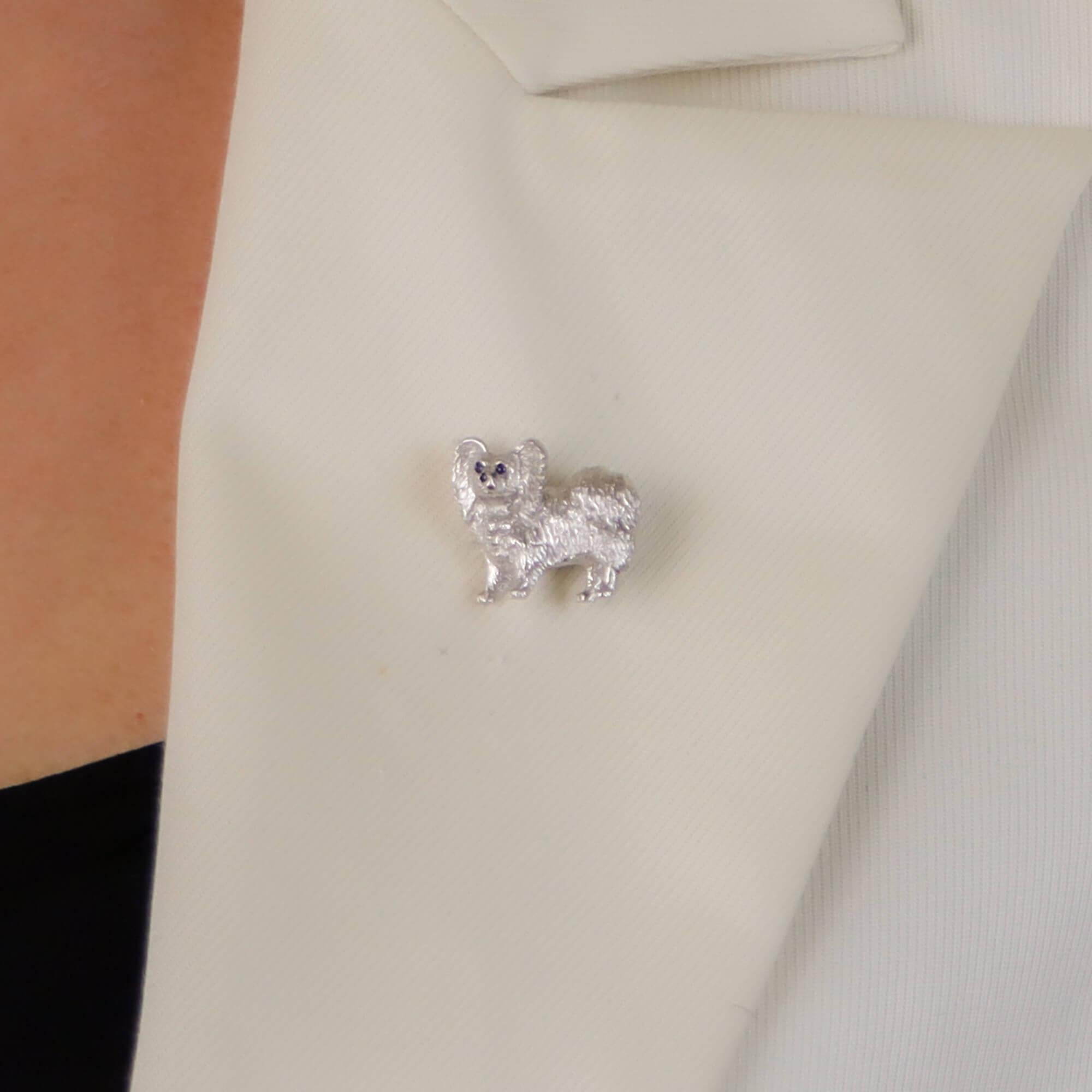 A beautiful sapphire and diamond Papillon dog pin brooch set in 18k white gold.

The brooch depicts a standing Papillon dog which is pavé set on the chest with 3 round brilliant cut diamonds. The dogs fur has been hand carved in 18k white gold to