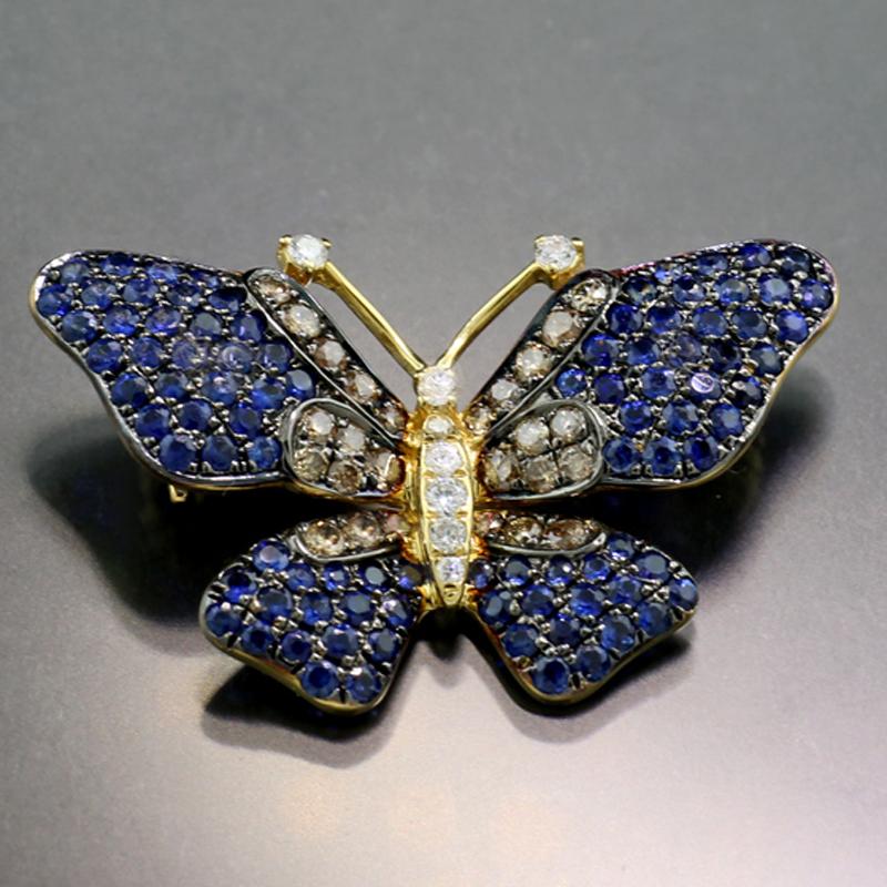 An Exquisite Butterfly adorned generously with 94 round faceted, deep blue sapphires totaling approximately 1.30 carats, and with 8 white diamonds (color grade: Wesselton) and 26 cognac-colored diamonds, all 34 full-cut natural diamonds totaling