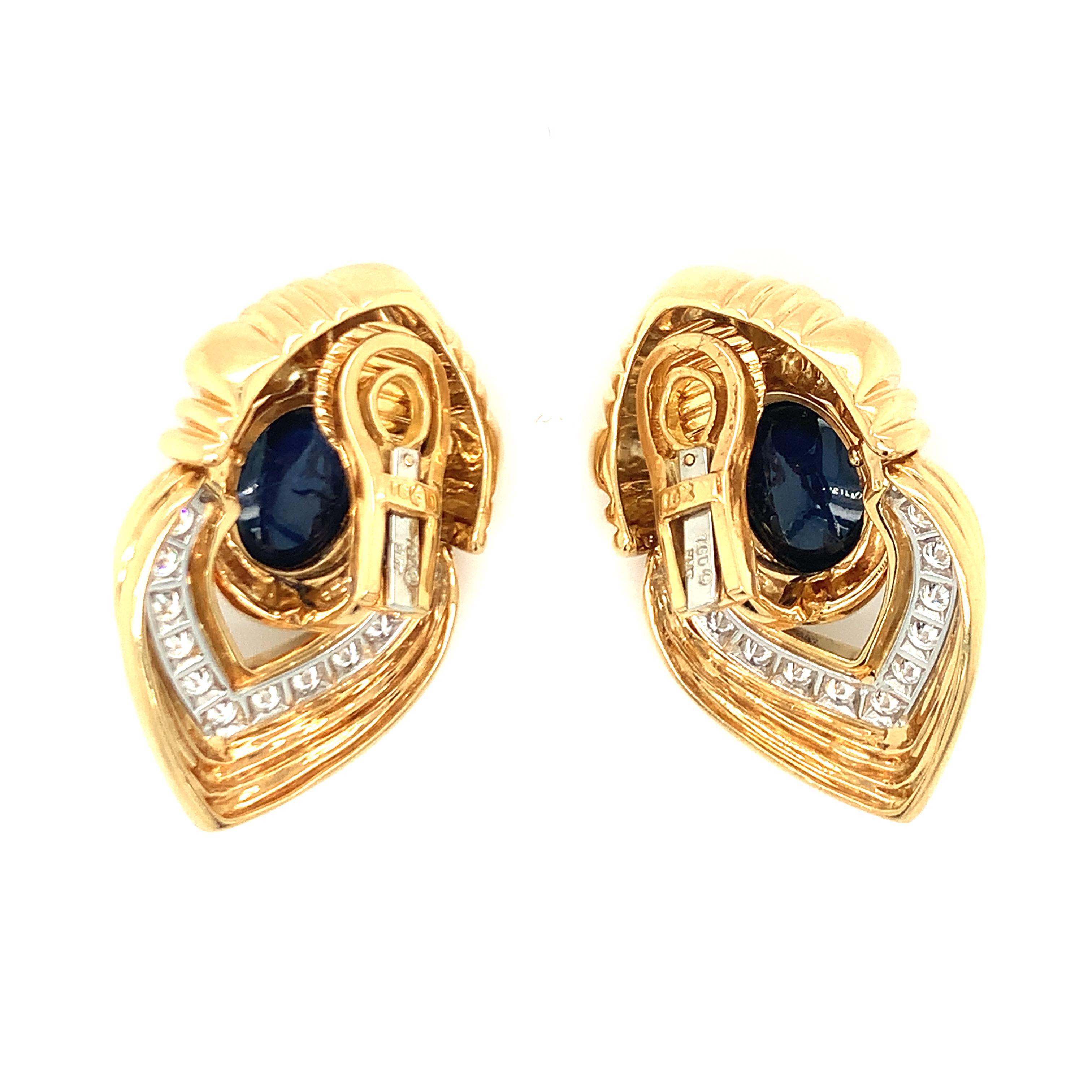 One pair of sapphire and diamond platinum and 18K yellow gold earclips featuring two bezel set, oval cabochon cut blue sapphires weighing 12 ct. in total (6 ct. each). The earrings feature a fluted door-knocker design accented with 26 round
