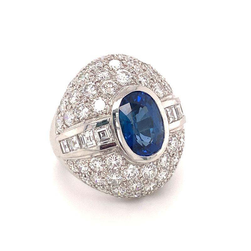 One sapphire and diamond platinum bombe ring centering one bezel set, oval brilliant cut sapphire weighing 3.50 ct. surrounded by 68 princess and round brilliant cut diamonds totaling 6.50 ct. Measures 26 millimeters long on top portion. Circa