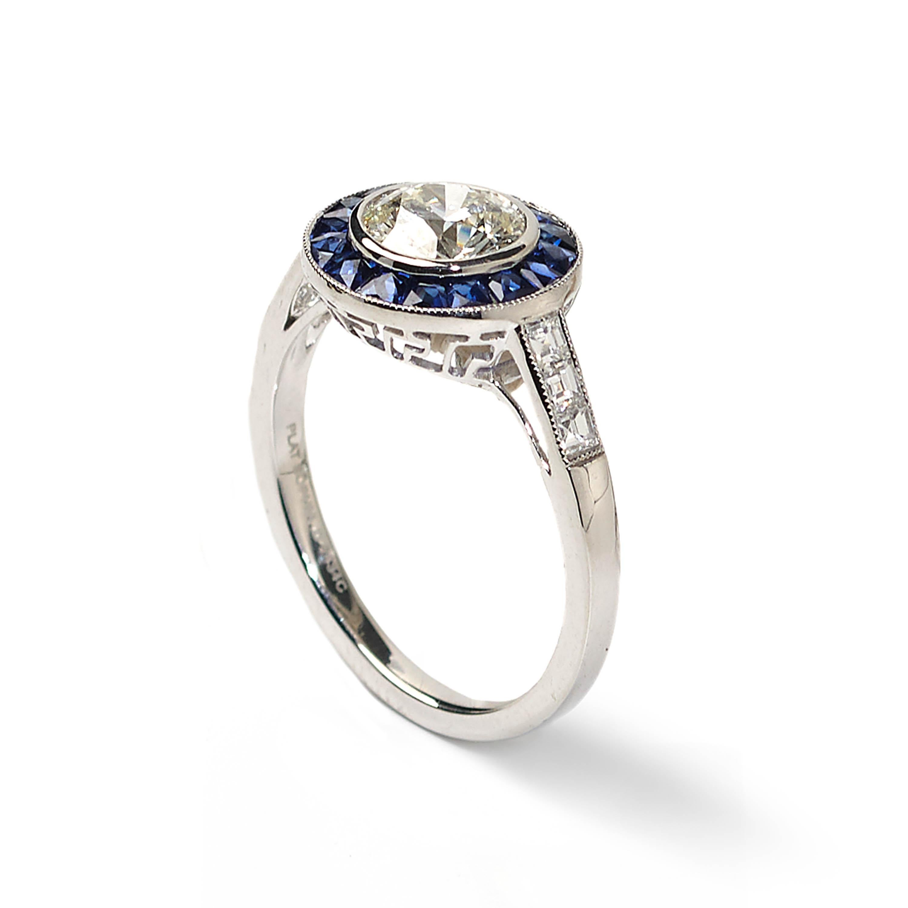 A modern halo design cluster ring set with a central round diamond weighing 1.00 carat, surrounded by a border of blue sapphires weighing a total of 0.68 carats, with diamond set shoulders weighing a total of 0.24 carats, mounted in platinum.