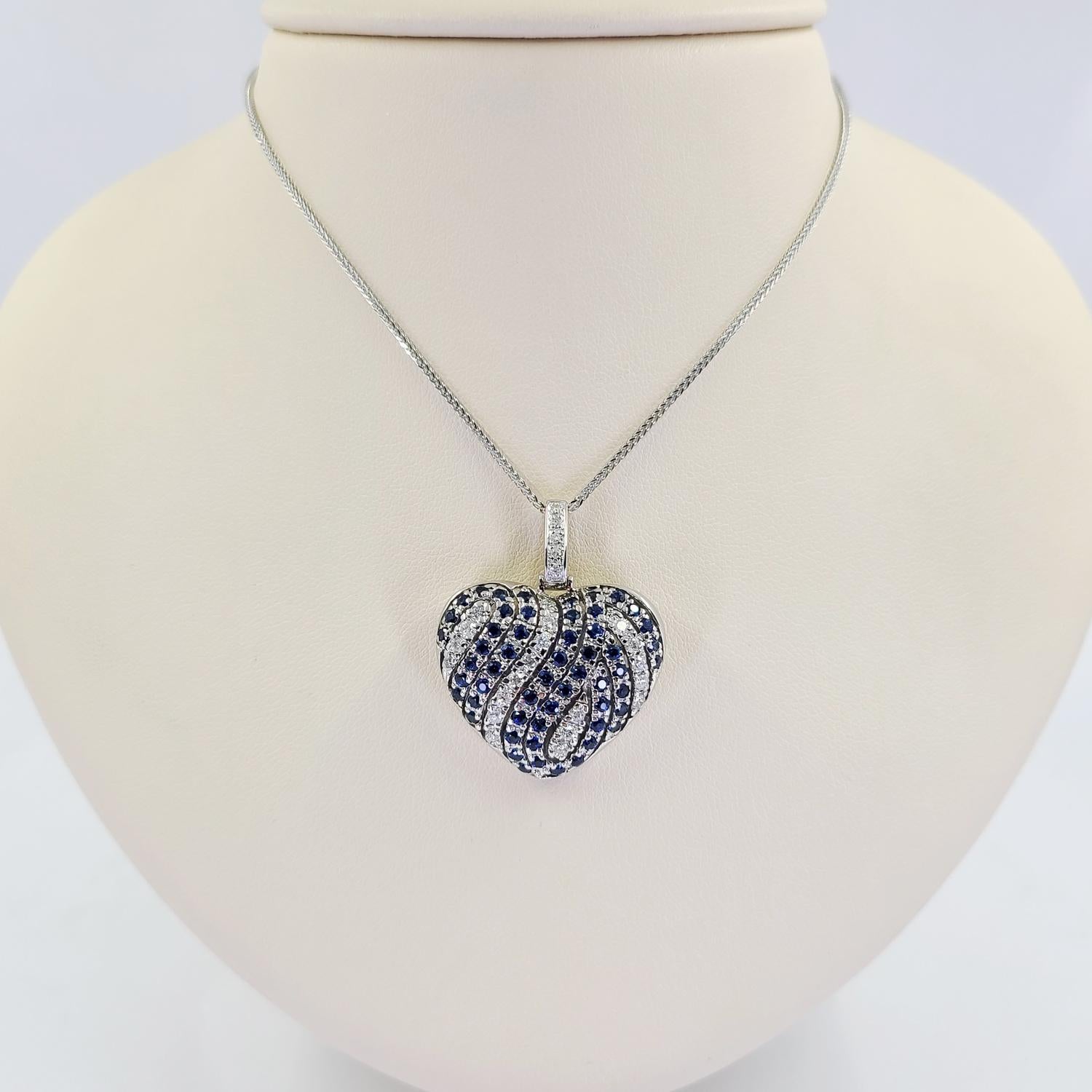 14 Karat White Gold Puffed Swirl Heart Pendant Necklace Featuring 25 Round Brilliant Cut Diamonds of SI Clarity and H/I Color Totaling 0.50 Carats Accented By 54 Round Sapphires Totaling Approximately 1.00 Carat. 16 Inch Chain with 1.4 Inch Slide