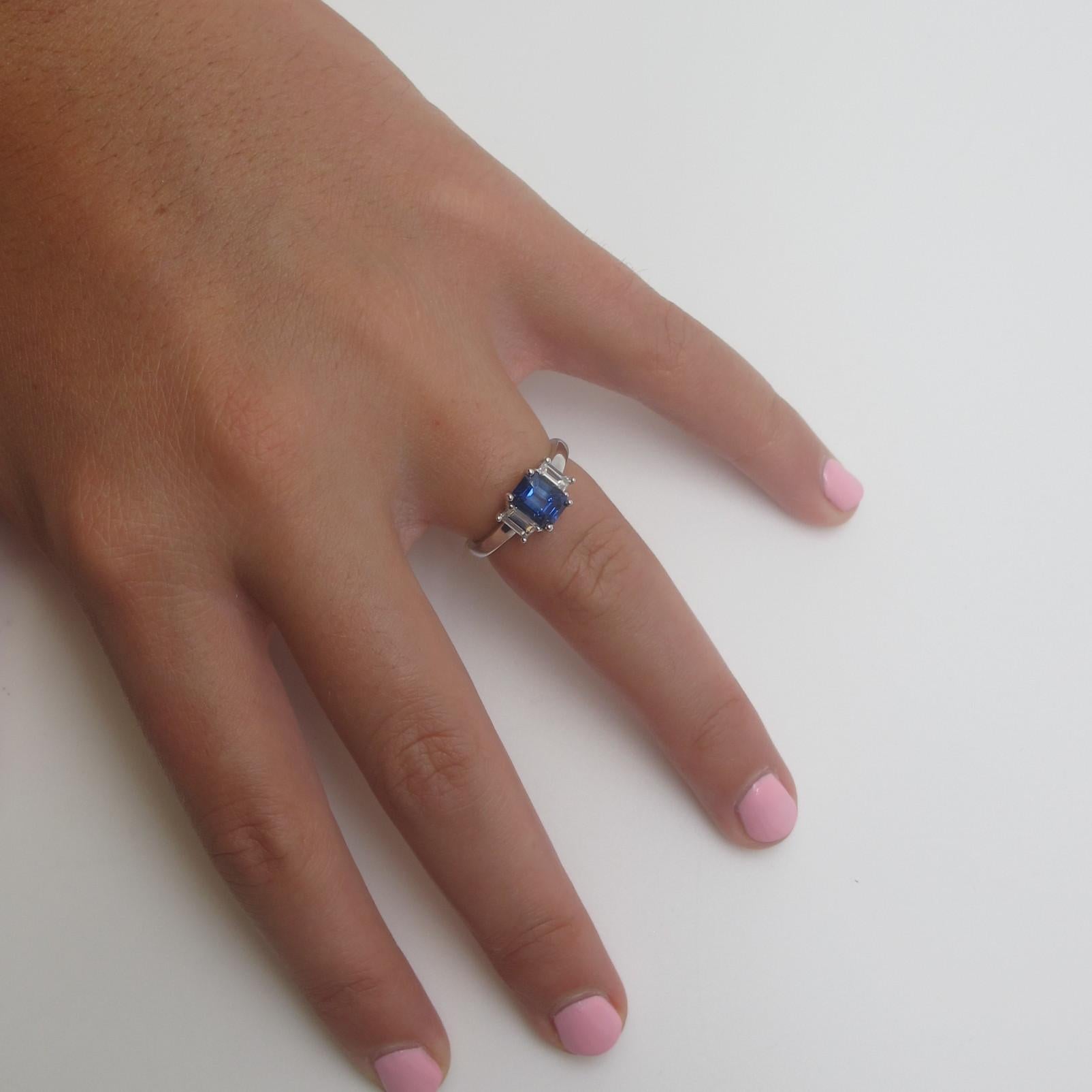 A beautiful, royal blue sapphire (7.05x5.36x4.08mm/1.49 carats) is featured in this classic 3-stone ring.  it is emerald cut, which is unusual for sapphire and is flanked by 2 emerald cut diamonds (.52 carats total weight) with color grade 