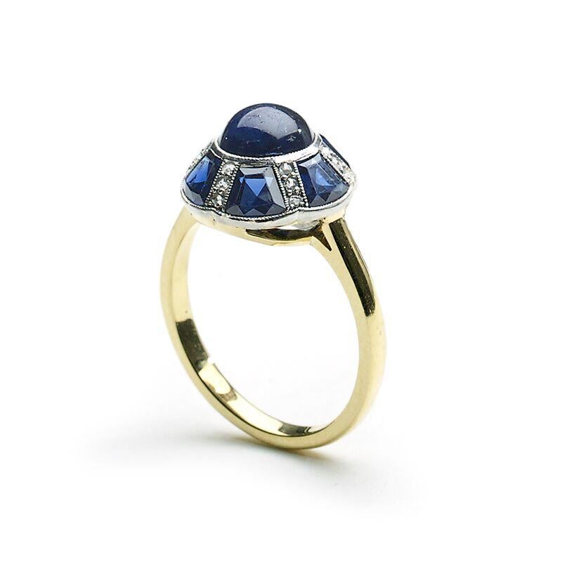 A sapphire and diamond ring, with a sapphire set circular domed cluster, with a cabochon-cut sapphire in the centre, surrounded by alternating fancy cut sapphires and sets of three rose-cut diamonds, mounted in silver-upon-gold, with millegrain