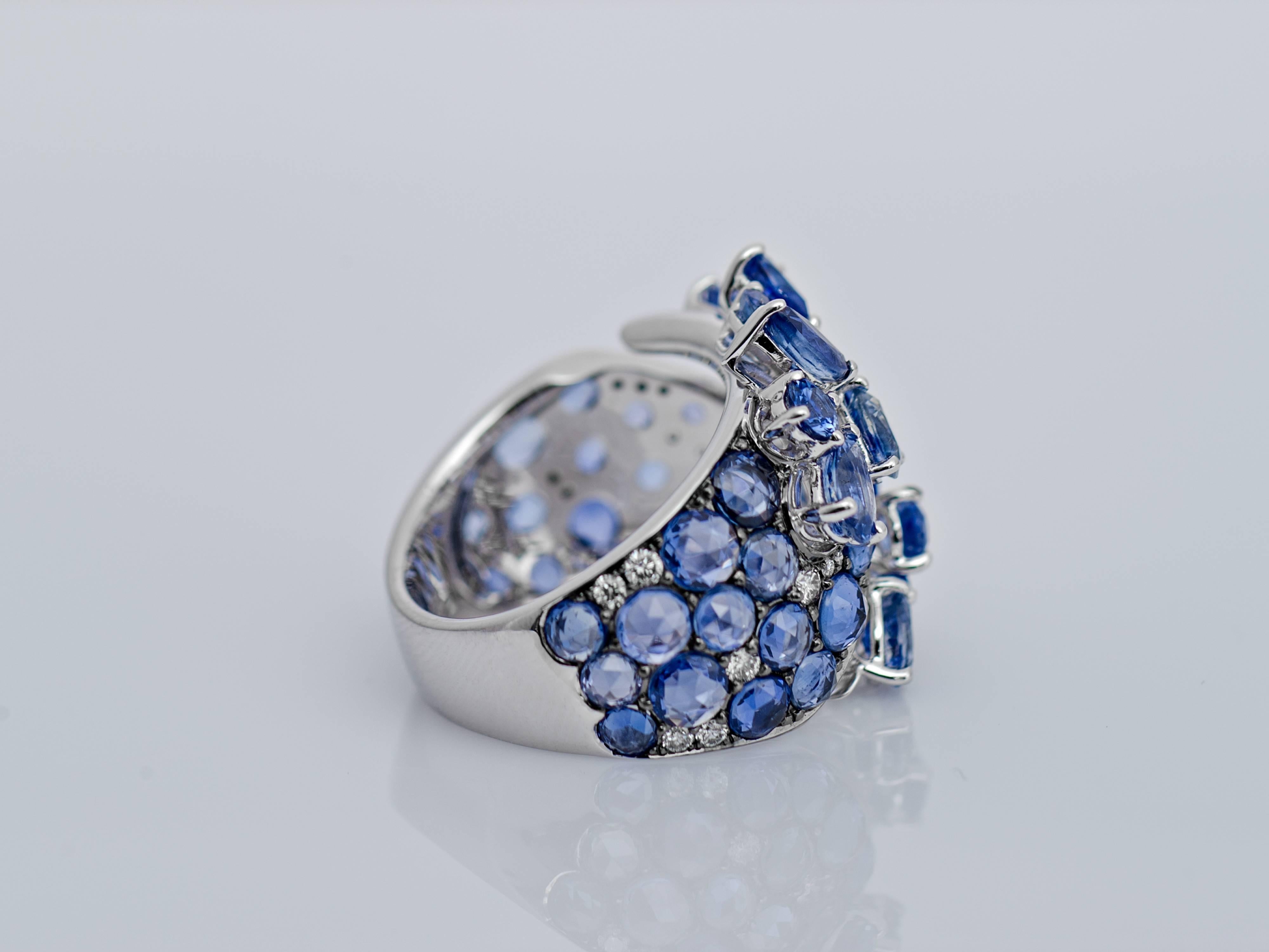 Designed as a stylised pair of flowers on top of a twisted ring leaving an intentional gap in the centre of the piece. Each flower head of cluster design set with pear and marquise shaped blue sapphires surrounded by more round sapphires and