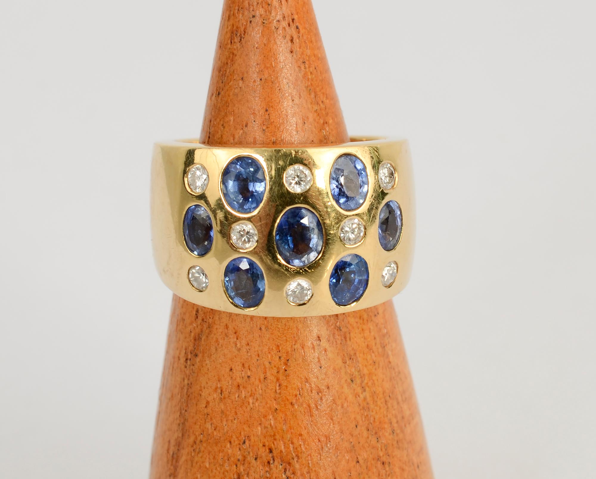 Stylish wide gold band ring with sapphires and diamonds. The 7 oval sapphires weigh a total of slightly more than one carat. Eight round diamonds weigh a total of slightly less than a carat. The ring is 7/16” wide in the front tapering to 5/16” at