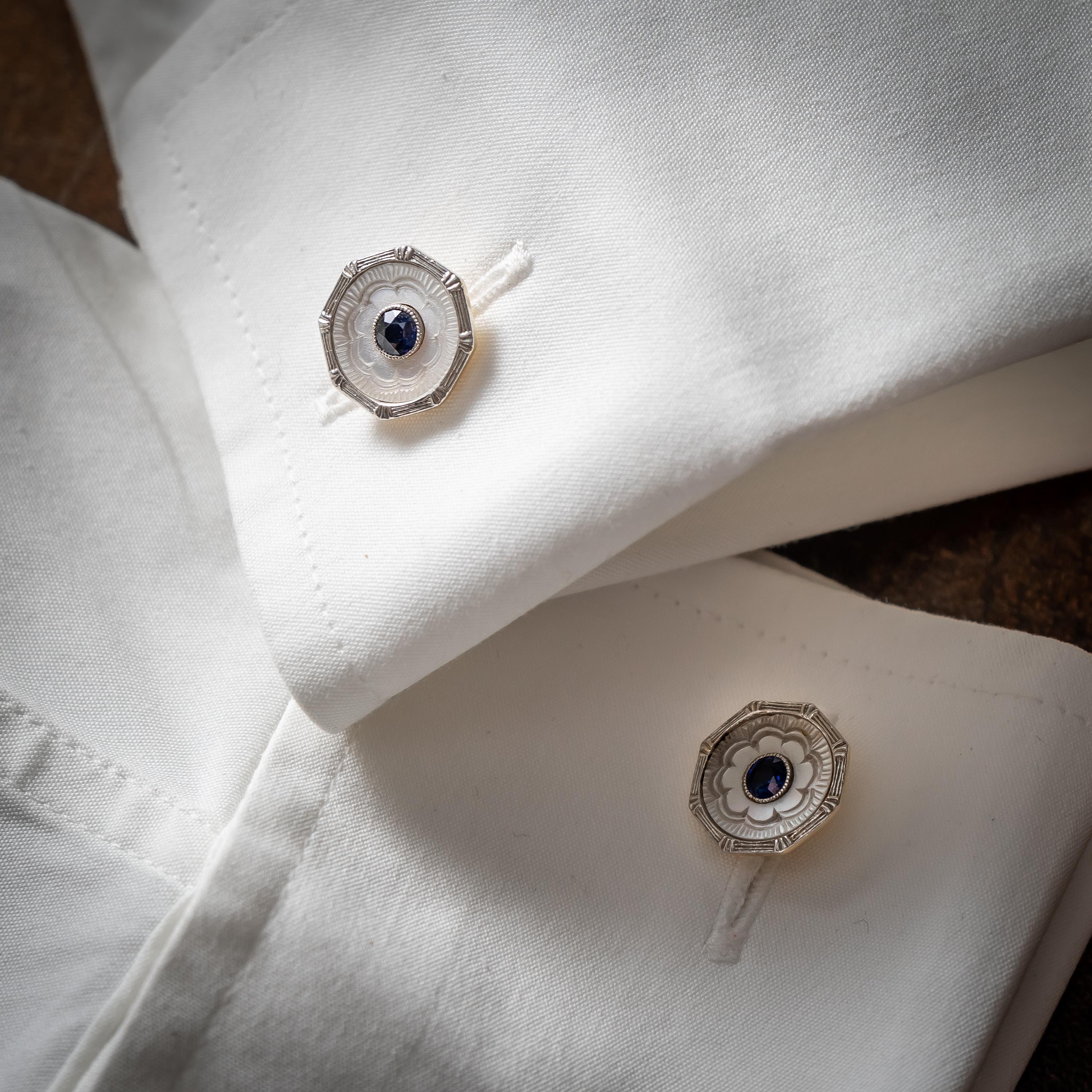 An Art Deco sapphire and mother-of-pearl dress-set, comprising a pair of cufflinks, with four buttons and three collar studs, with round, faceted sapphires in the centre, surrounded by carved mother of pearl, with engraved white gold octagonal