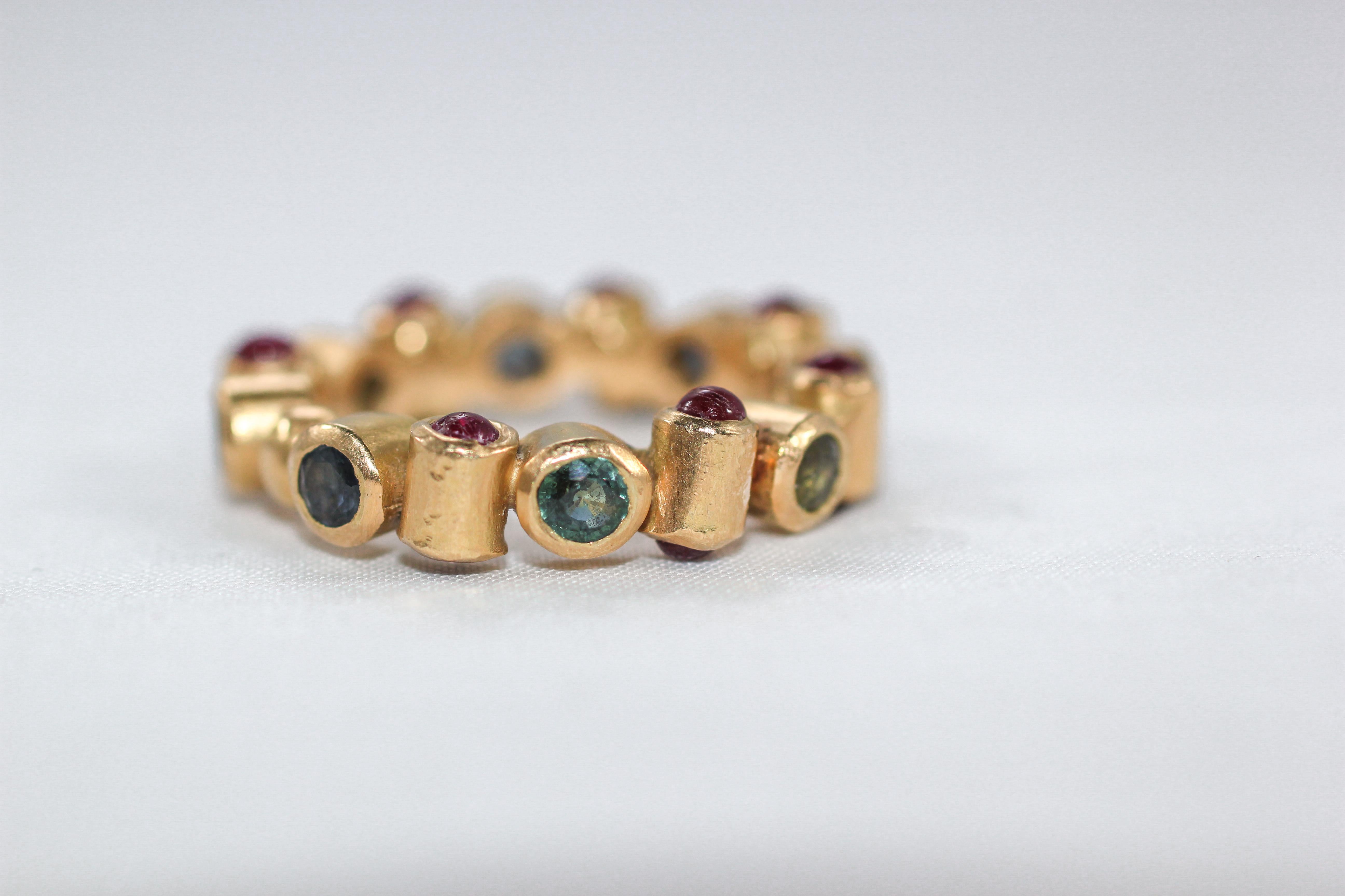 Cylinder Ring. An unusual 18K gold bezel bridal band ring is set on all three sides. On one side it displays untreated blue sapphires, brilliant-cut stones. Ruby cabochons are set on the top and the bottom. Like a sculpture, it appears slightly