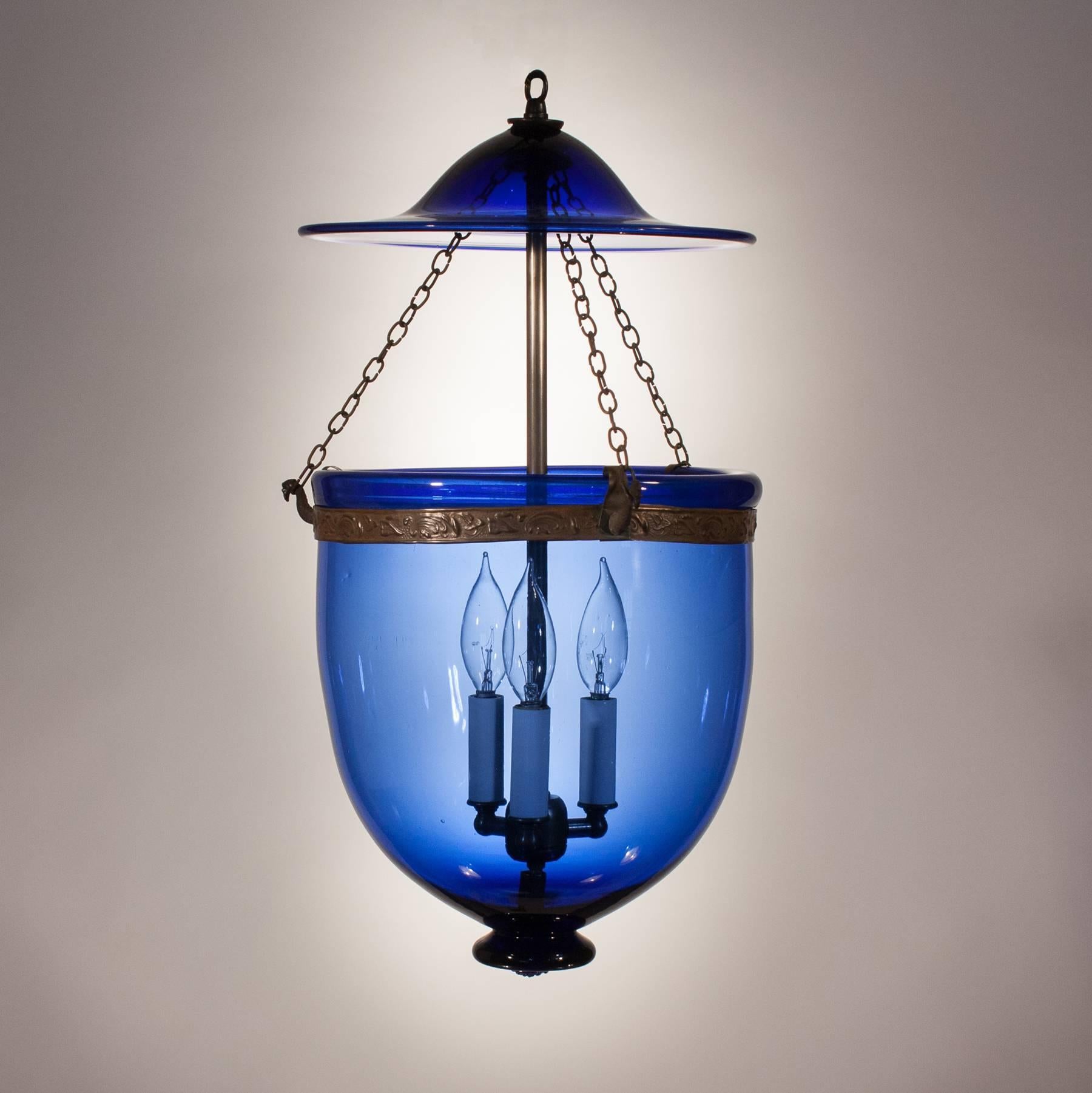 The brilliant sapphire blue and classic contours of this 19th century handblown glass bell jar lantern make it a real gem in our collection. The hall lantern has its original smoke bell and brass band with a flowing leaf motif that adds just the