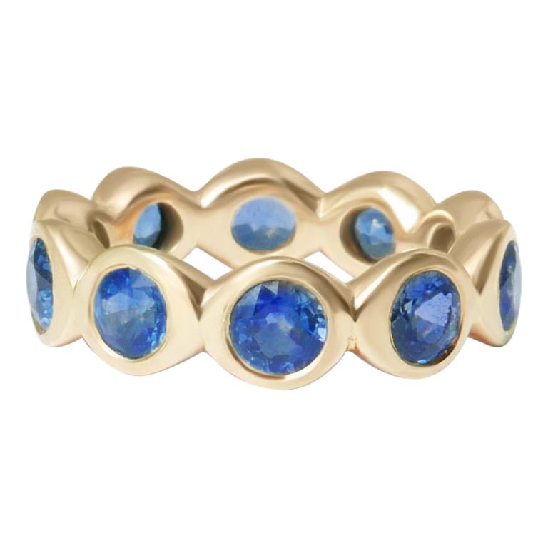 Crafted in solid 14-karat yellow gold, this substantial eternity band features ten round brilliant cut blue sapphires.  This ring is a UK size L 1/2 (equivalent to US size 5 7/8).  The total carat weight of the ten 4mm natural Sri Lankan blue