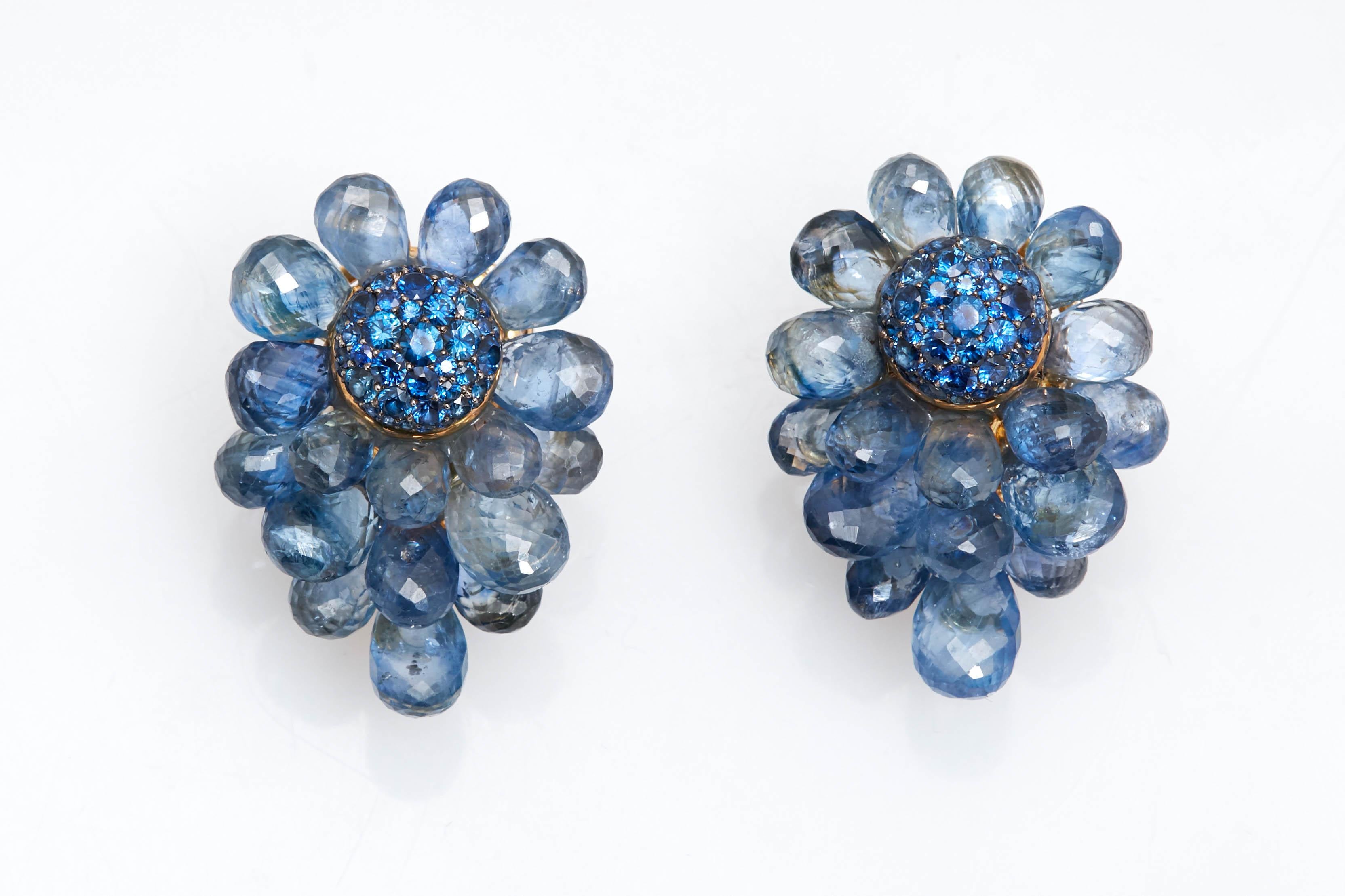 A chic pair of gold, sapphire briolette and sapphire cluster earclips.
18 kt., centering circular domes encrusted with round sapphires, within overlapping petals of 34 sapphire briolettes, with maker's mark, made in the USA circa 1960. 